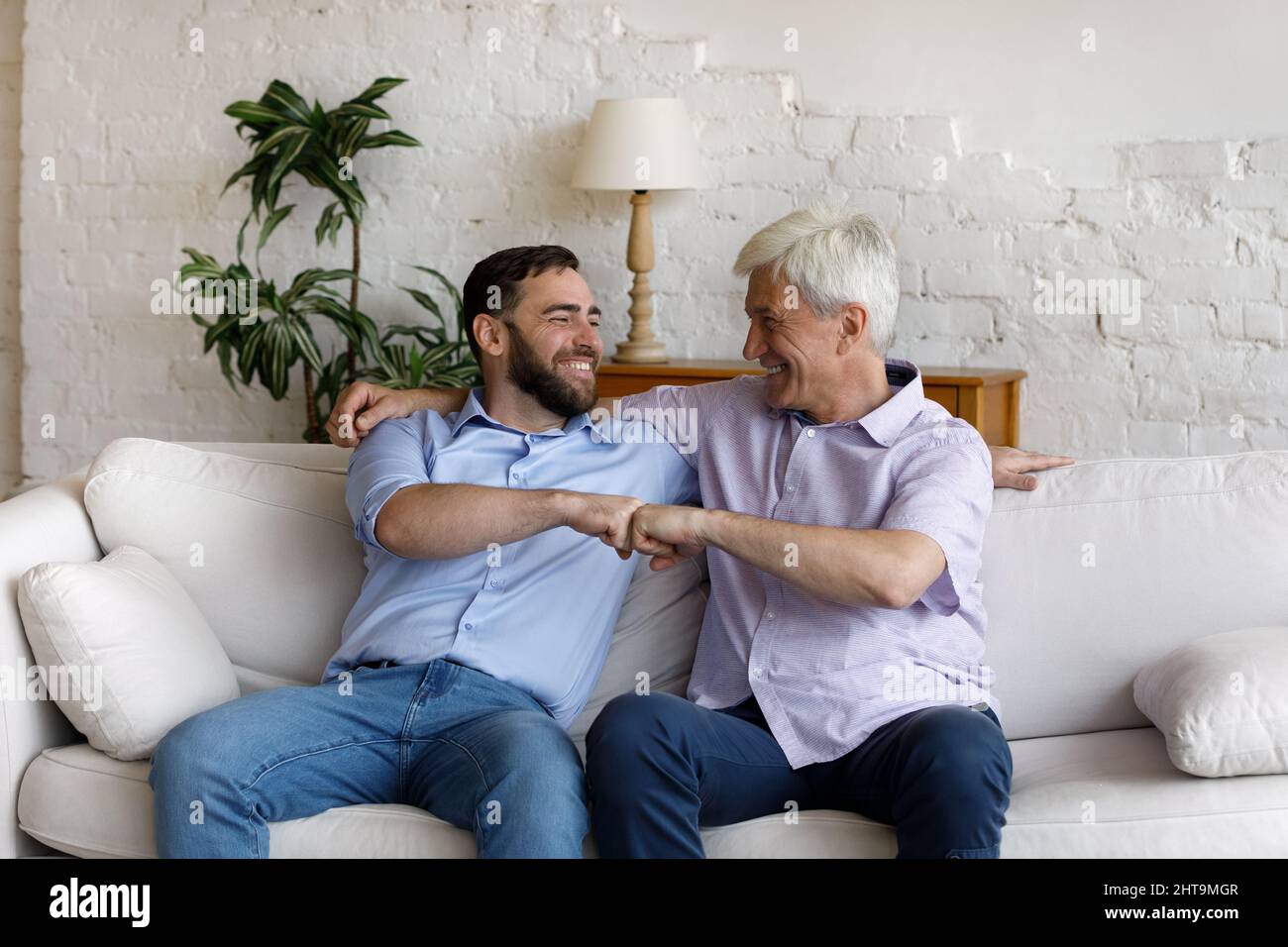 Ältere und jüngere Männer sitzen auf dem Sofa und machen Faustschlag Stockfoto