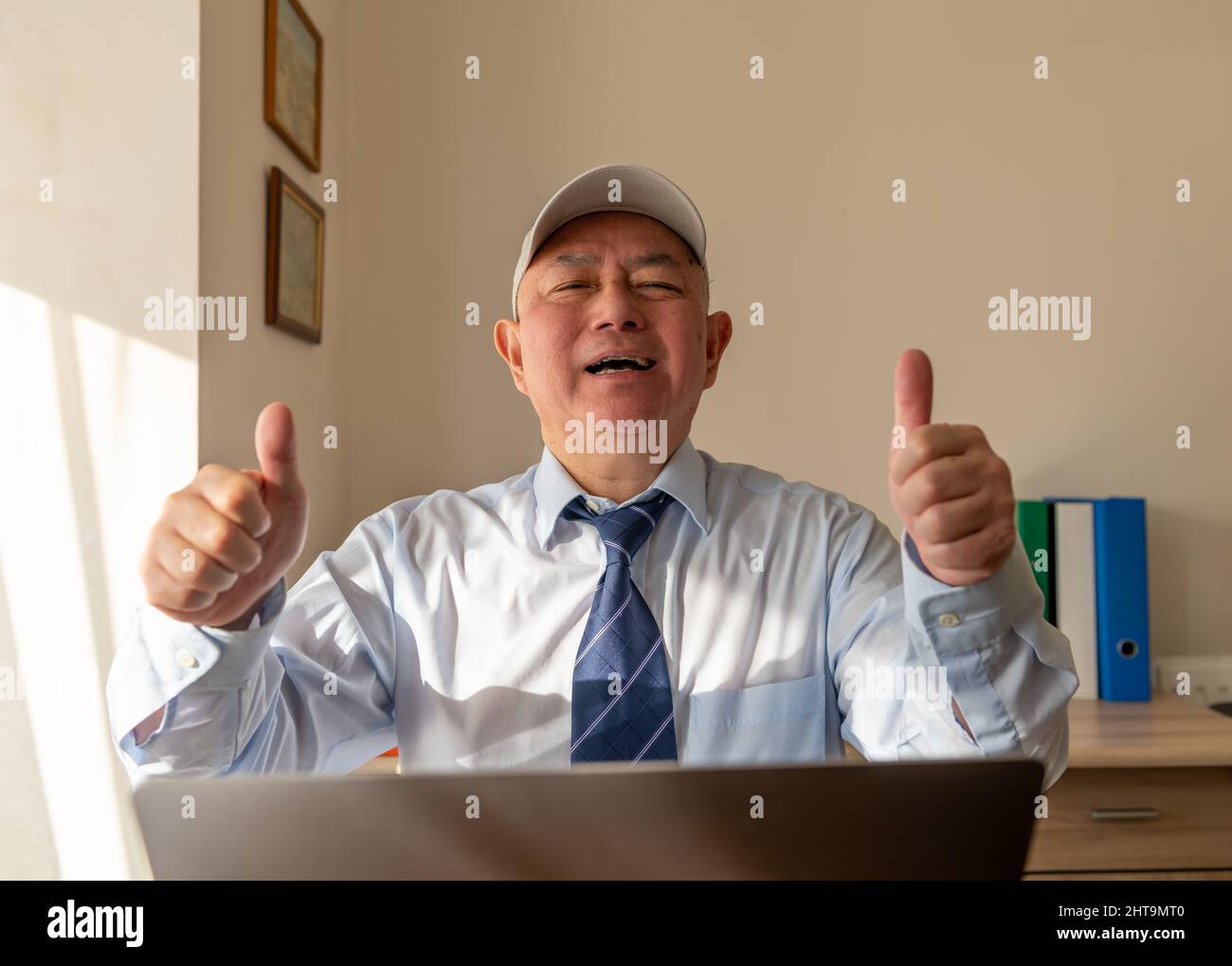 Ein leitender Angestellter im Büro gab nach Abschluss einer großen Online-Vereinbarung mit einem Lächeln das Daumen nach oben. Stockfoto