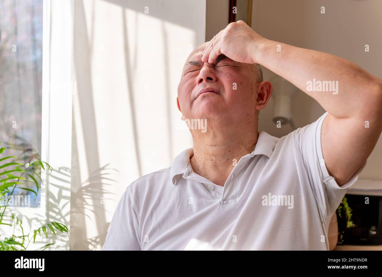Ein gereifter älterer Mann zu Hause kneift und reibt seinen Kopf, fühlt sich unwohl und oder hat Schmerzen. Gefühl Unwohlsein Konzept. Stockfoto