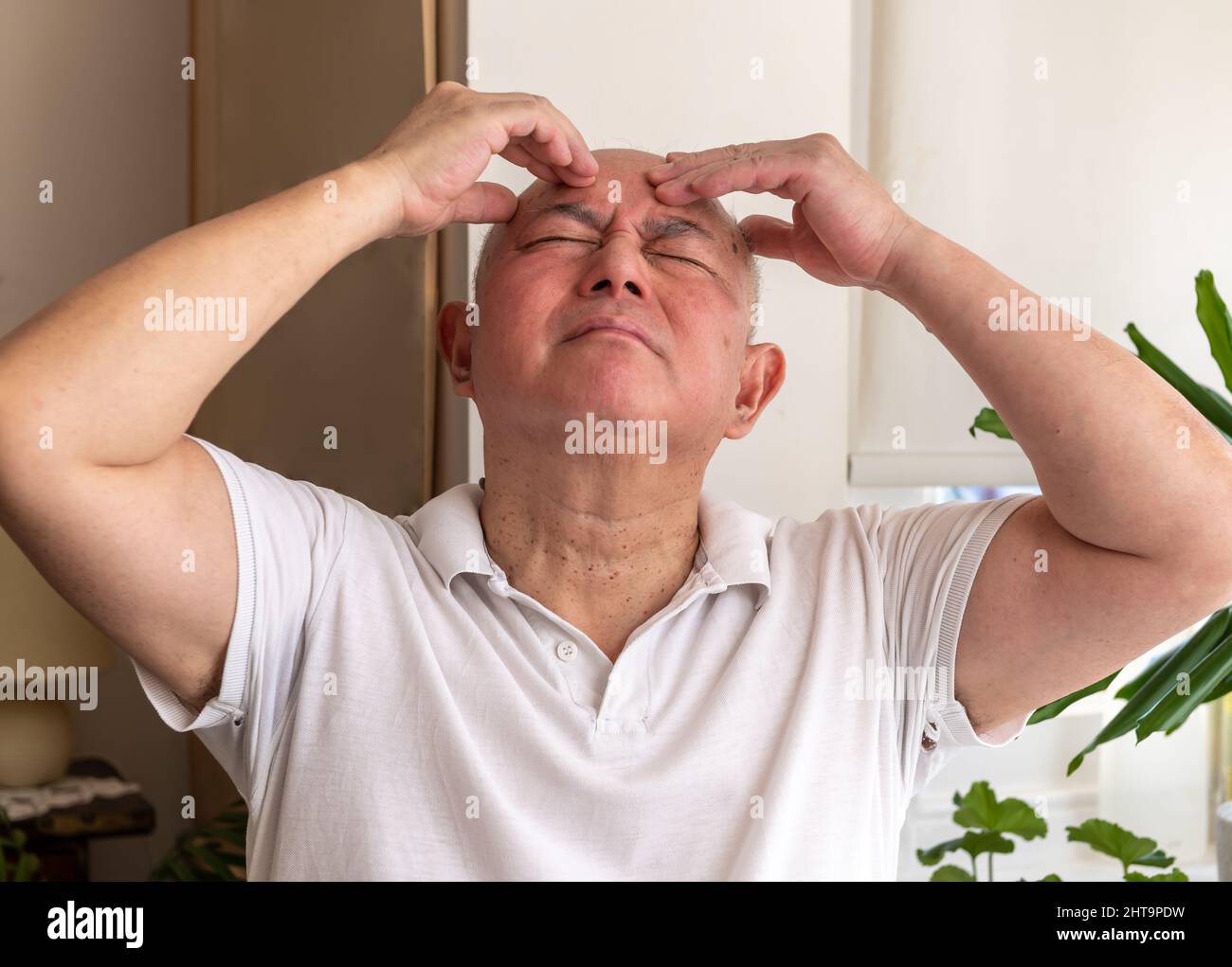 Ein gereifter älterer Mann zu Hause kneift und reibt seinen Kopf, fühlt sich unwohl und oder hat Schmerzen. Gefühl Unwohlsein Konzept. Stockfoto