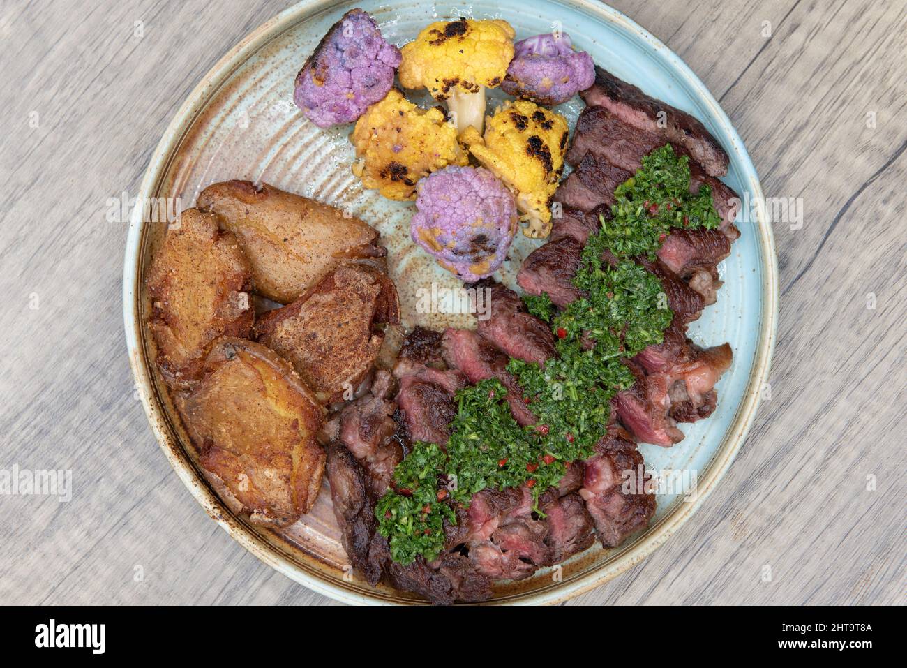 Blick von oben auf den vollen Teller mit gegrilltem Ribeye-Steak, gebratenen Kochbananen und bunten Blumenkohlbissen als komplette Mahlzeit. Stockfoto