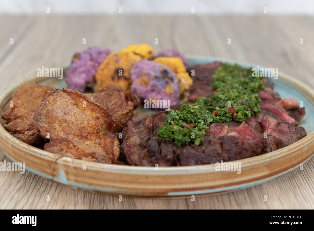 Ein voller Teller mit gegrilltem Ribeye-Steak, gebratenen Kochbananen und bunten Blumenkohlbissen zum Essen als komplette Mahlzeit. Stockfoto