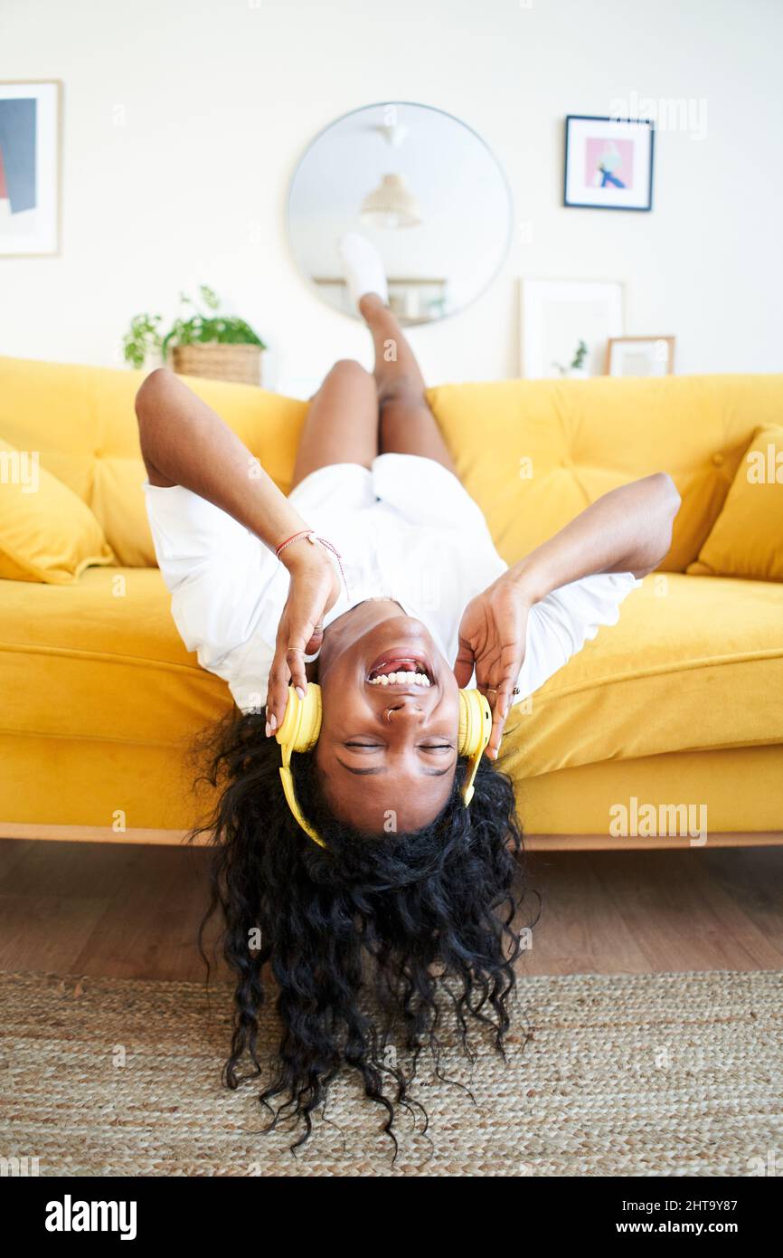 Vertikales Foto einer motivierten jungen Frau, die zu Hause mit Kopfhörern auf dem Sofa Musik hört. Stockfoto