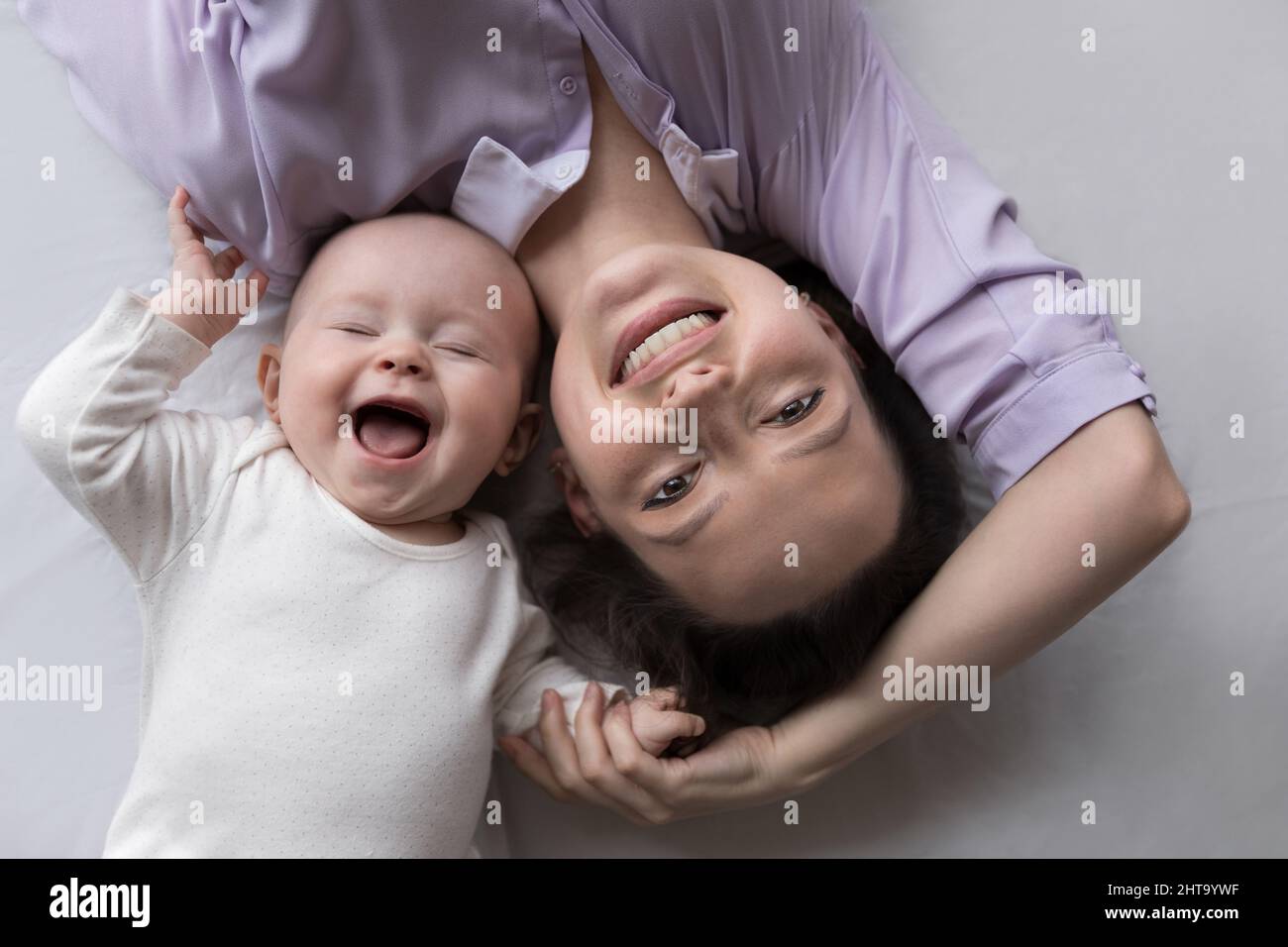 Glückliche Mutter und ein paar Monate Baby, das sich auf einem großen Bett ausruhte Stockfoto