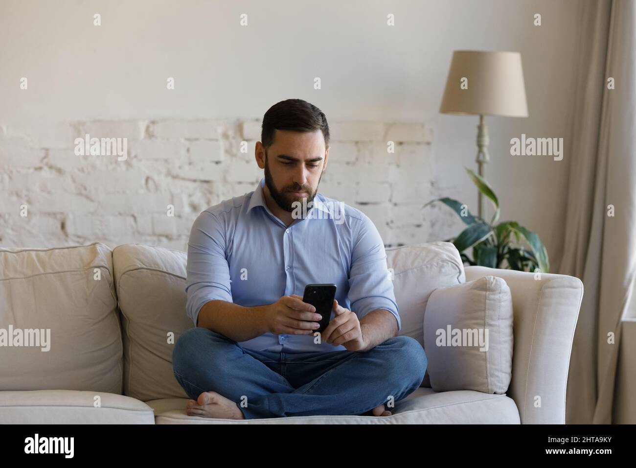 Millennial Mann sitzt auf der Couch im Wohnzimmer hält Smartphone Stockfoto