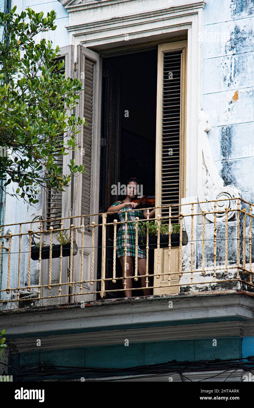Die junge Frau praktiziert die Geige in einer gewölbten Tür von der Vorderseite ihres Hauses in Havanna, Kuba. Stockfoto