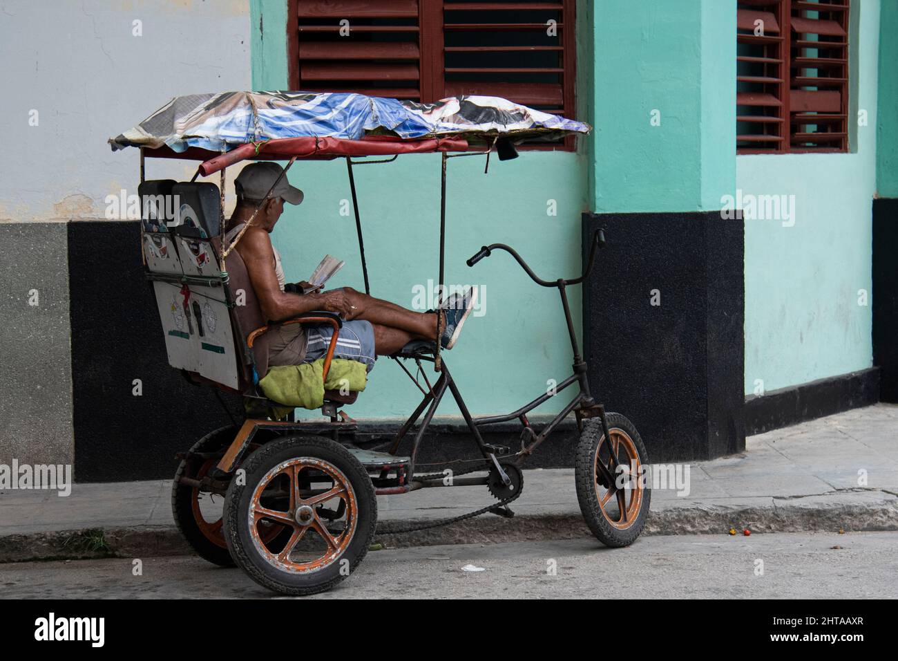 Ein Mann, der in seinem Fahrradtaxi in Havanna, Kuba, ein Buch liest. Stockfoto