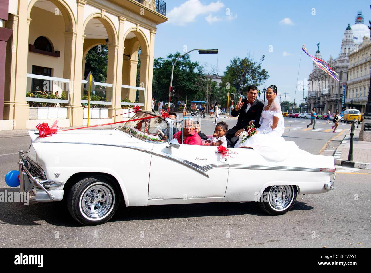 Die kubanische Braut und Gruppe sitzen lächelnd auf einem alten Oldtimer, während sie auf einer Autofahrt auf dem Prado Boulevard in Havanna, Kuba, mehr als nur einen Katzensprung machen. Stockfoto