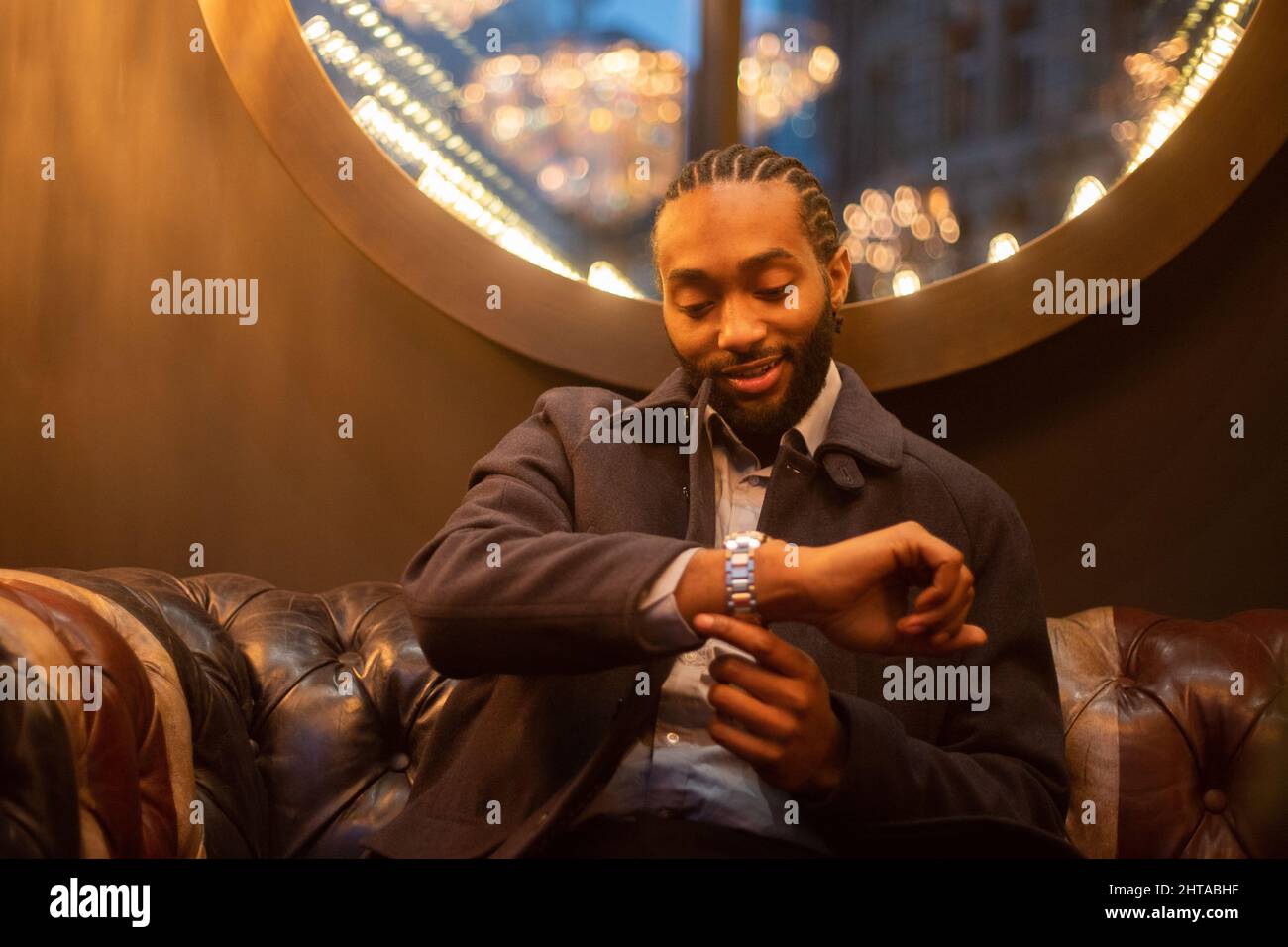 Geschäftsmann überprüft die Zeit auf seiner Armbanduhr, glücklicher erfolgreicher Mensch in Innenräumen Stockfoto