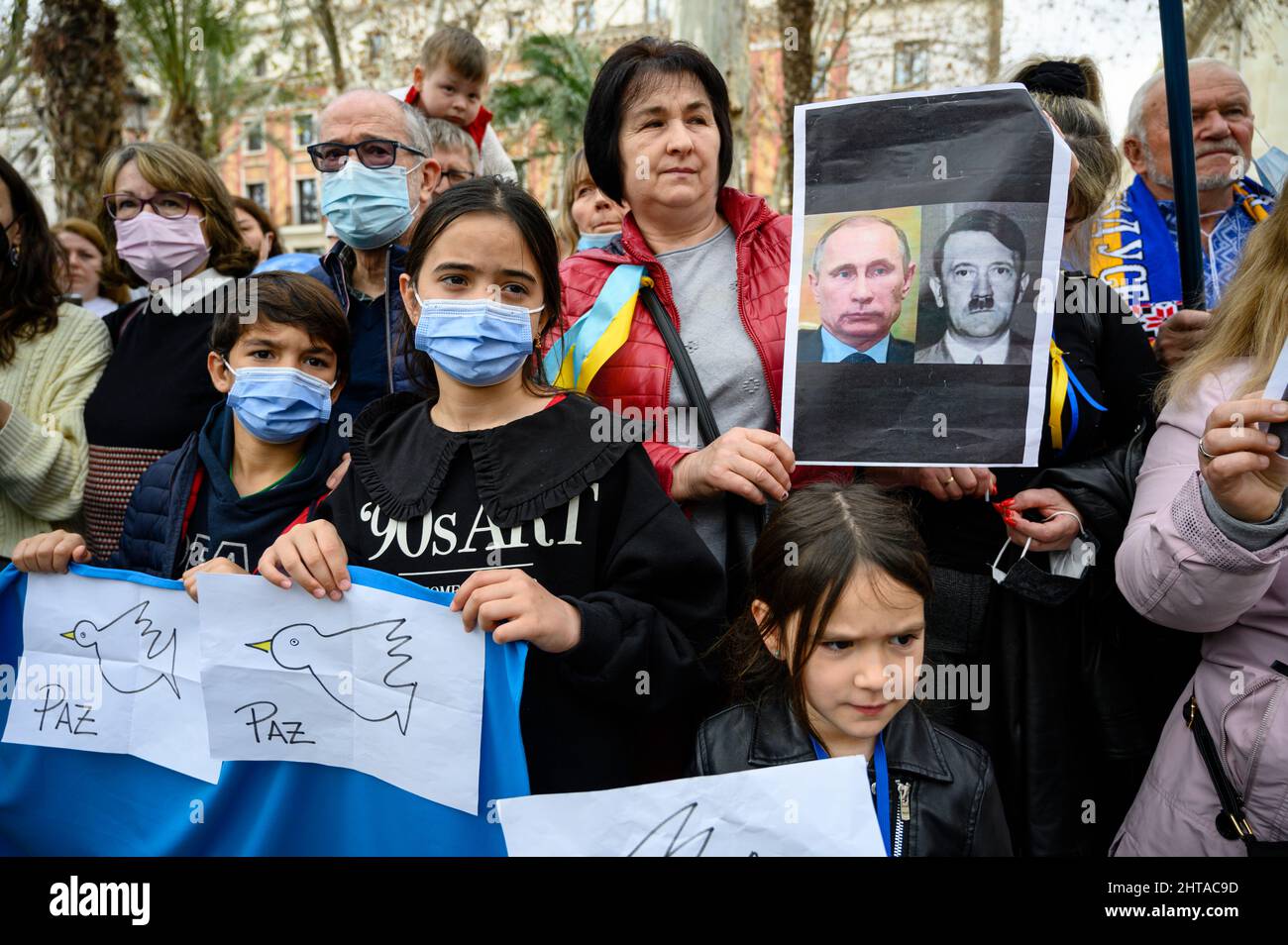 Sevilla, Spanien. 27.. Februar 2022. Eine ukrainische Frau hält ein Transparent, das den russischen Präsidenten Wladimir Putin mit Adolf Hitler vergleicht, während verschiedene Kinder eine ukrainische Flagge und Papiere mit dem Wort „Frieden“ auf Spanisch halten. Ukrainische Bürger, die in Sevilla leben, demonstrierten, um ihr Land und ihre Regierung zu unterstützen und gegen die russische Invasion und Wladimir Putin. (Foto: Ángel García/Pacific Press/Sipa USA) Quelle: SIPA USA/Alamy Live News Stockfoto