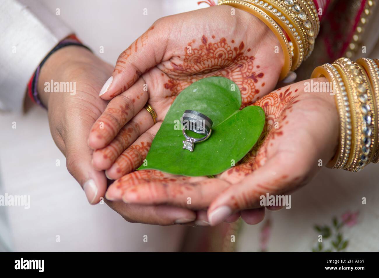 Nahaufnahme einer Braut und eines Bräutigams, die ihre Eheringe auf einem Blatt mit Henna an den Händen der Braut halten Stockfoto