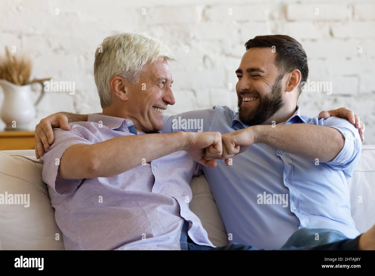 Glücklicher älterer Mann, sein Sohn, auf dem Sofa sitzend, hat eine Faust gebumt Stockfoto