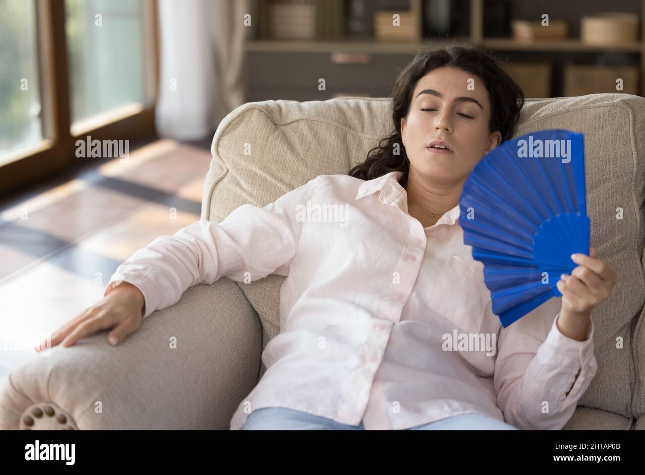 Gestresste tausendjährige hispanische Frau fühlt sich zu Hause überhitzt. Stockfoto