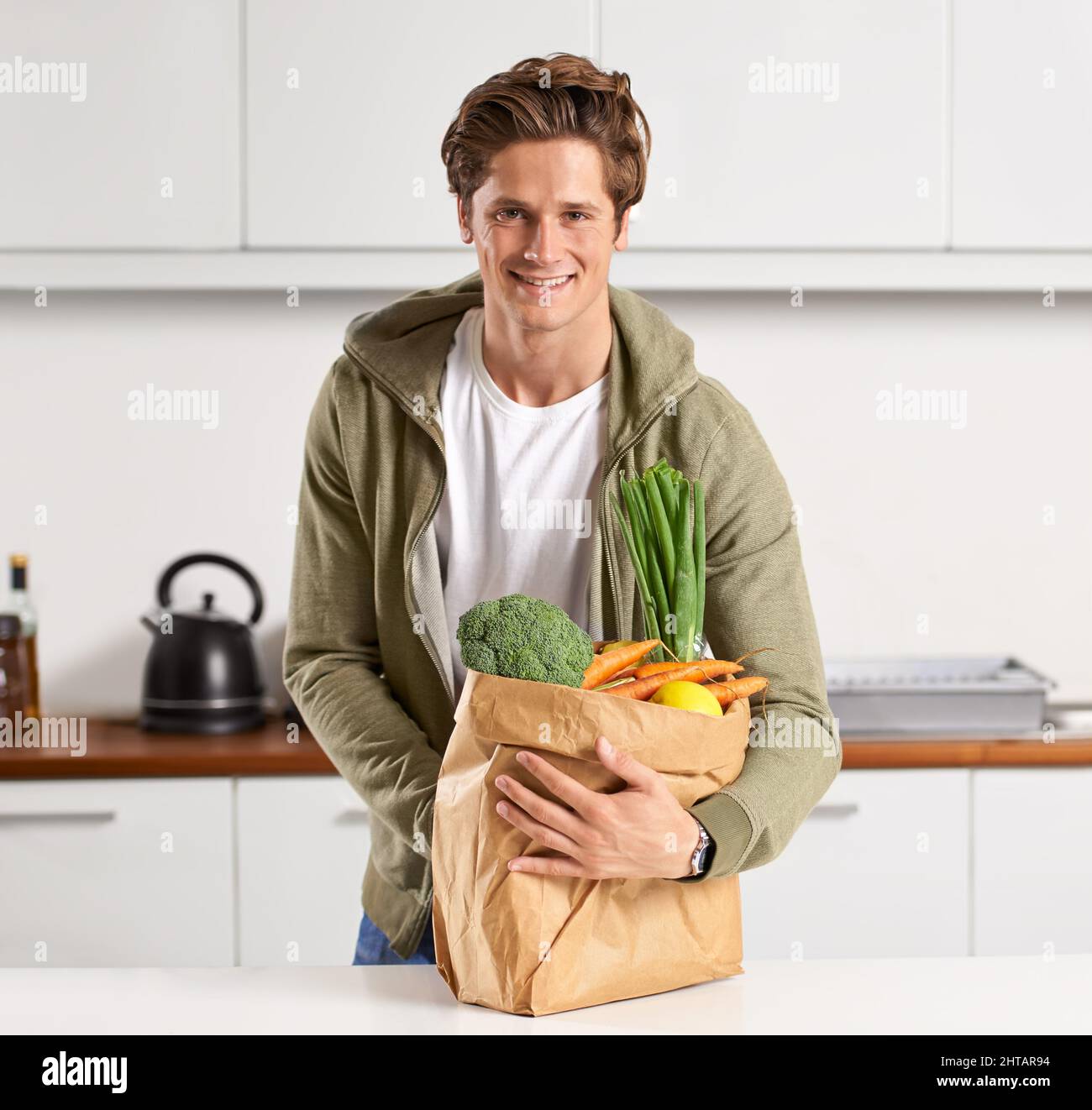 Ich bin stolz darauf, was in meinen Körper geht. Ein junger Mann in einer Küche, der einen braunen Papierbeutel mit Gemüse hält. Stockfoto