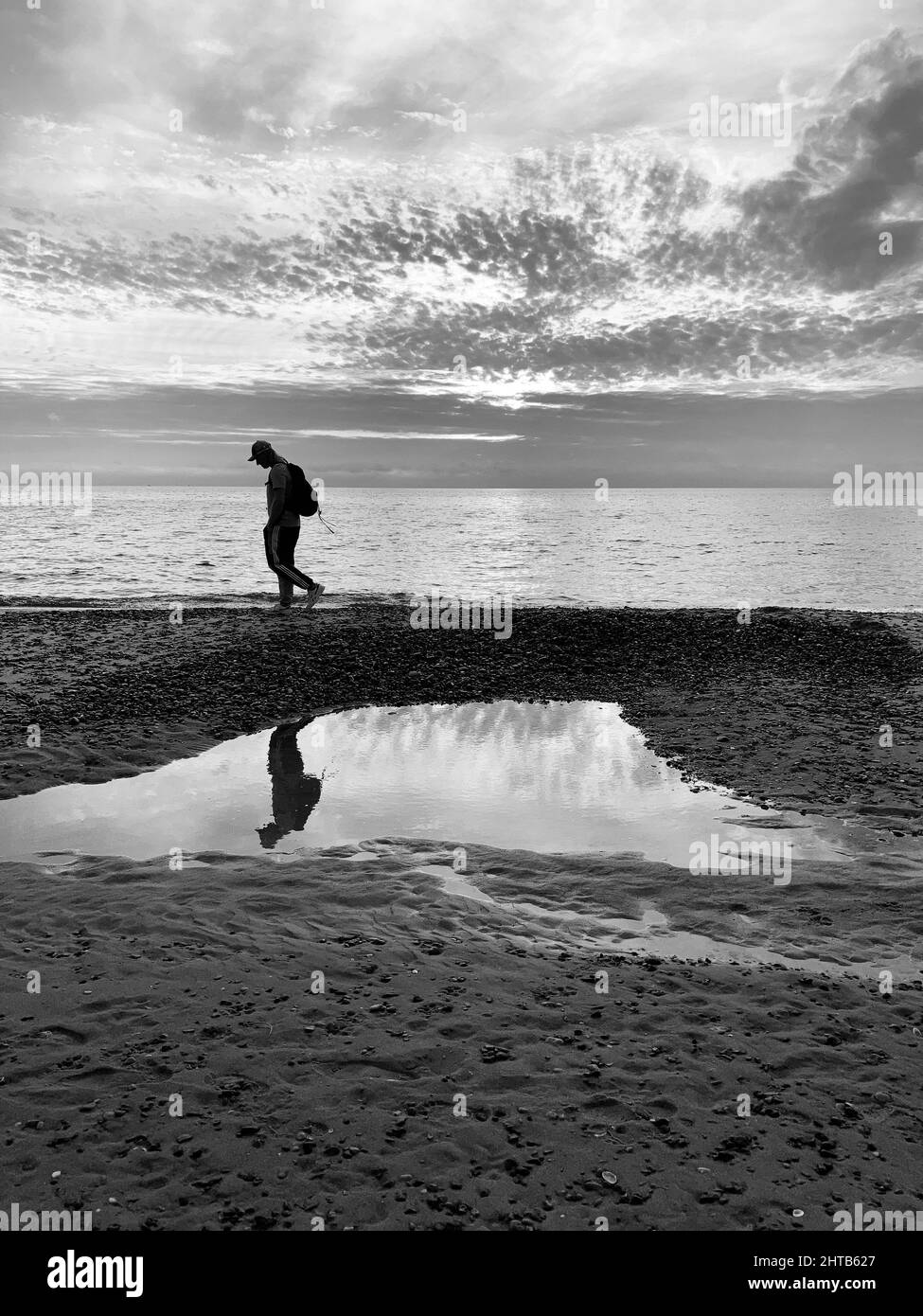 Vertikale Aufnahme eines Mannes, der am Strand entlang in der Nordsee mit einer Spiegelung in Schwarz und Weiß geht Stockfoto