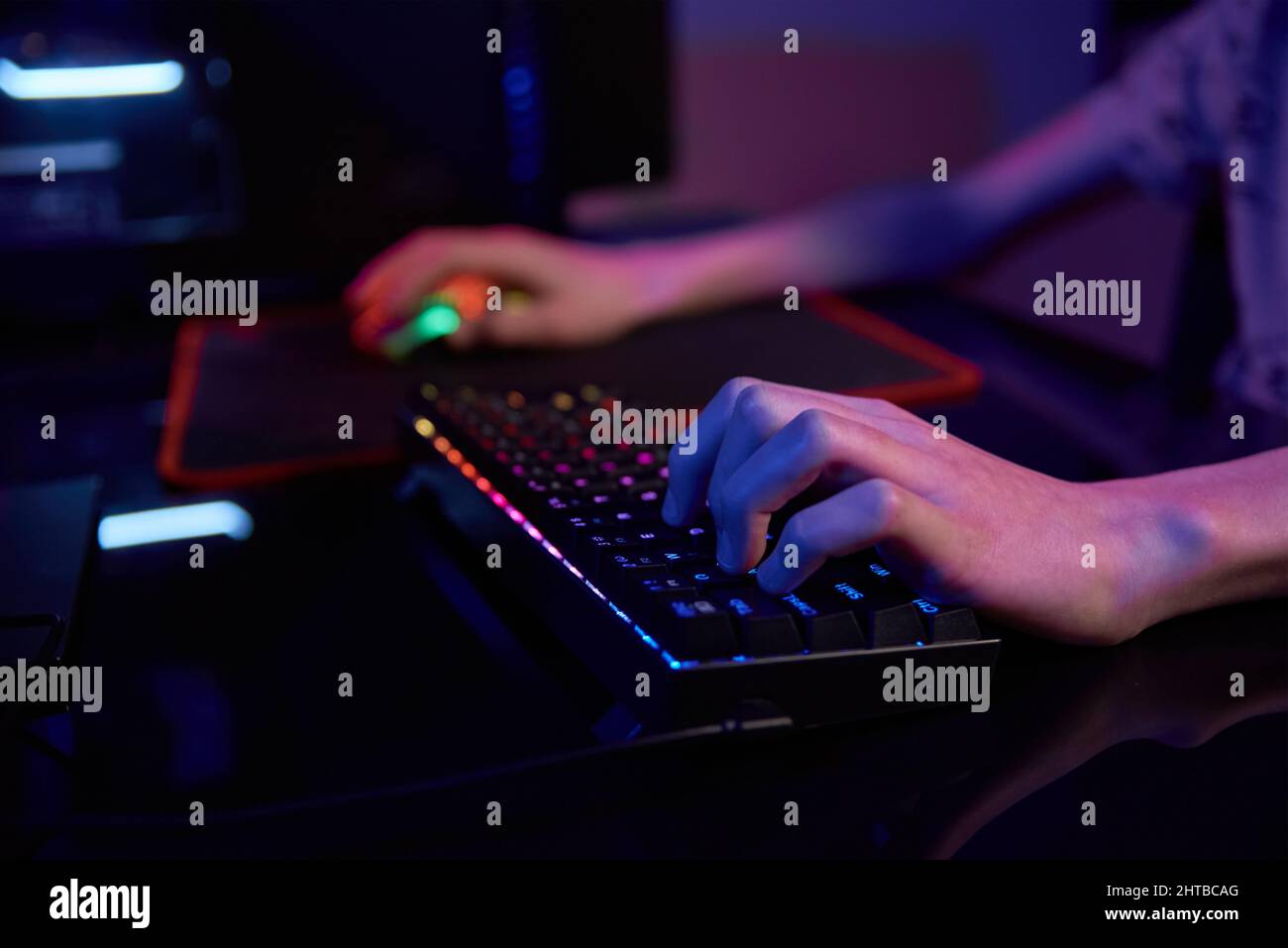 Teenaeger Junge spielen Computer-Videospiel in dunklen Raum, verwenden neonfarbene rgb mechanische Tastatur, Ort für Cybersport-Gaming Stockfoto
