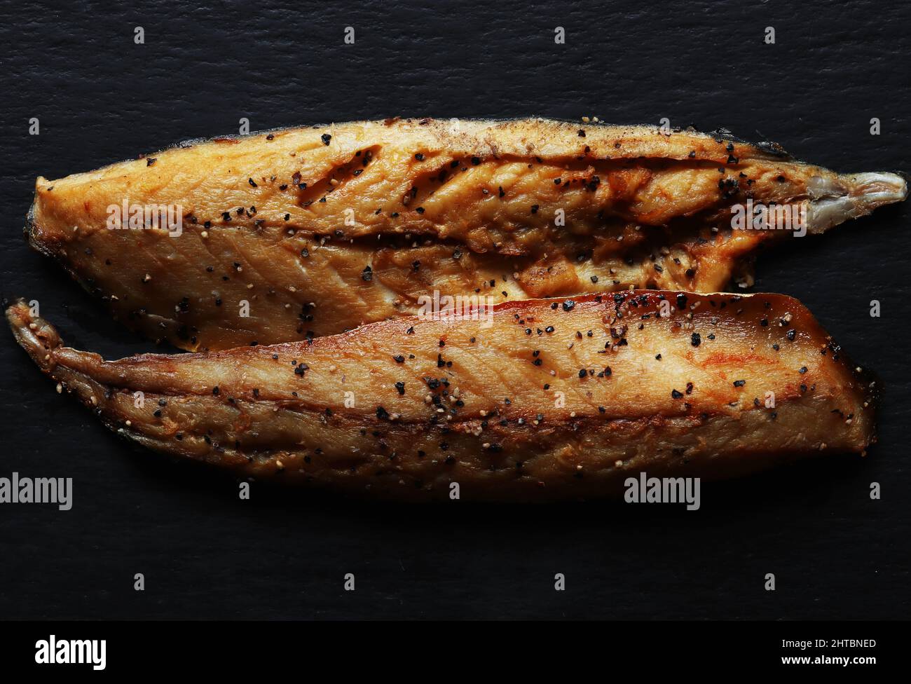 Draufsicht auf zwei Filets geräucherter Makrele mit gemahlenem schwarzem Pfeffer auf Schiefergrund Stockfoto