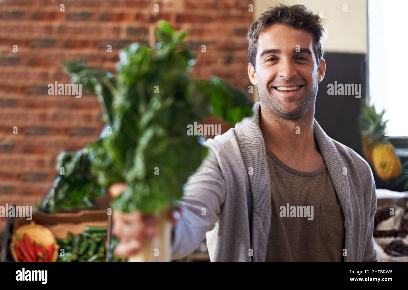 Es ist reich an Eisen. Porträt eines jungen Mannes in einem Lebensmittelgeschäft, der Spinat vor die Kamera hält. Stockfoto
