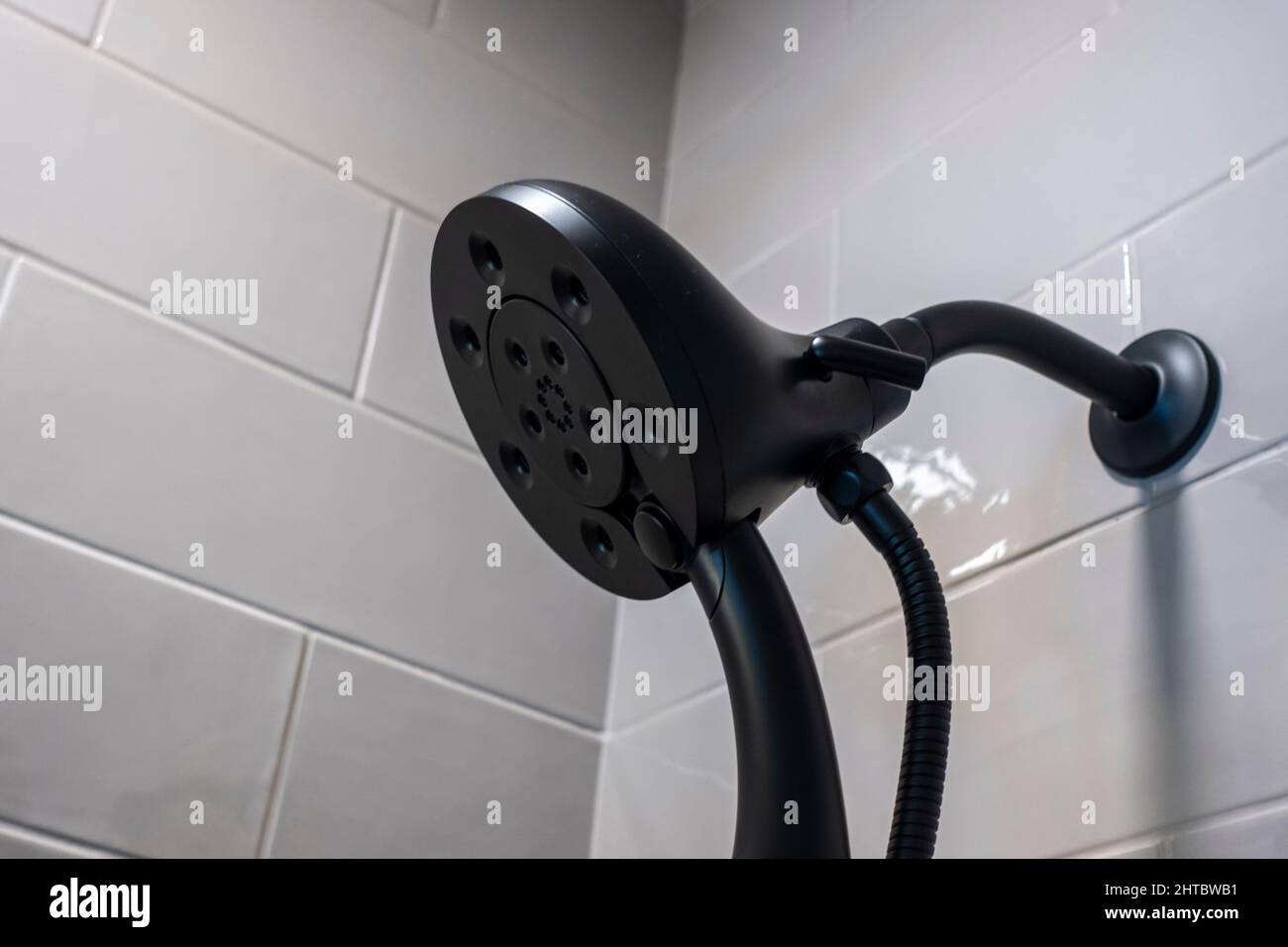 Nahaufnahme eines modernen abnehmbaren schwarzen Duschkopfes in einer weiß gefliesten Badewanne Stockfoto