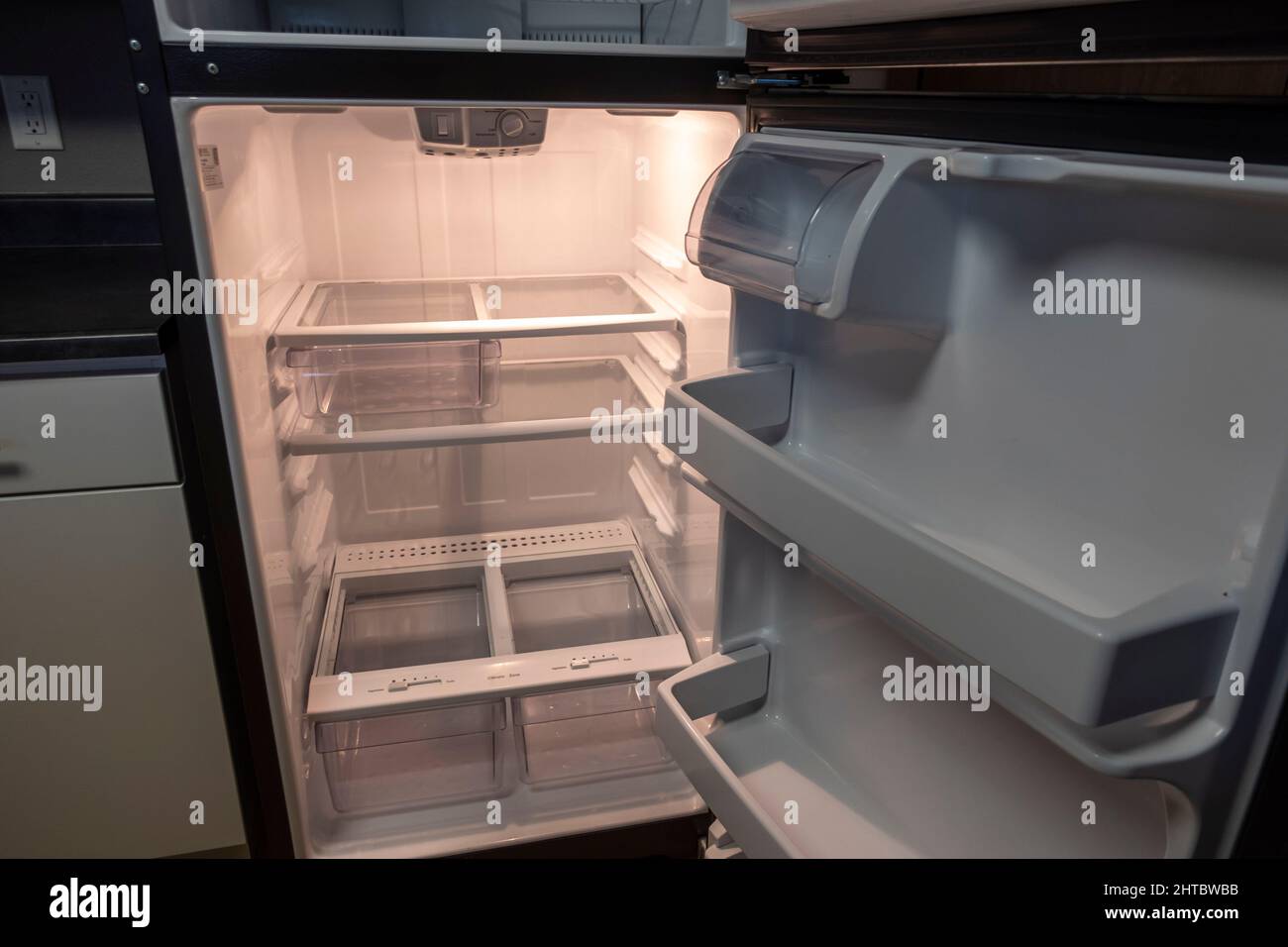 Blick auf einen weißen, leeren Kühlschrank mit weit geöffneter Tür, um mehrere Regale und Schubladen ohne Nahrung zu sehen Stockfoto