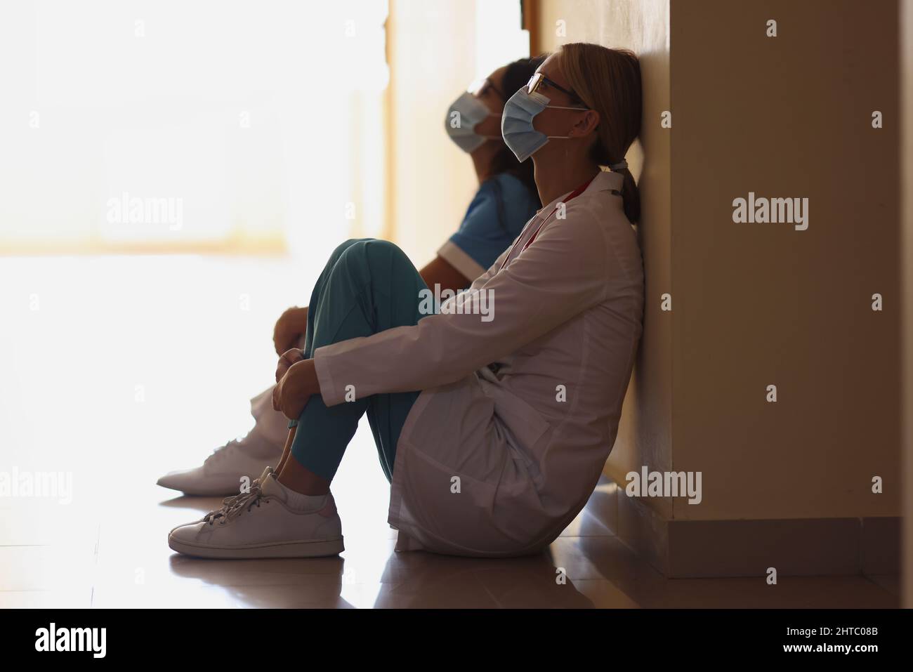 Erschöpfte Krankenschwestern nach einer harten langen Operation, die auf dem Boden in der Halle saß, schwierige Schicht Stockfoto