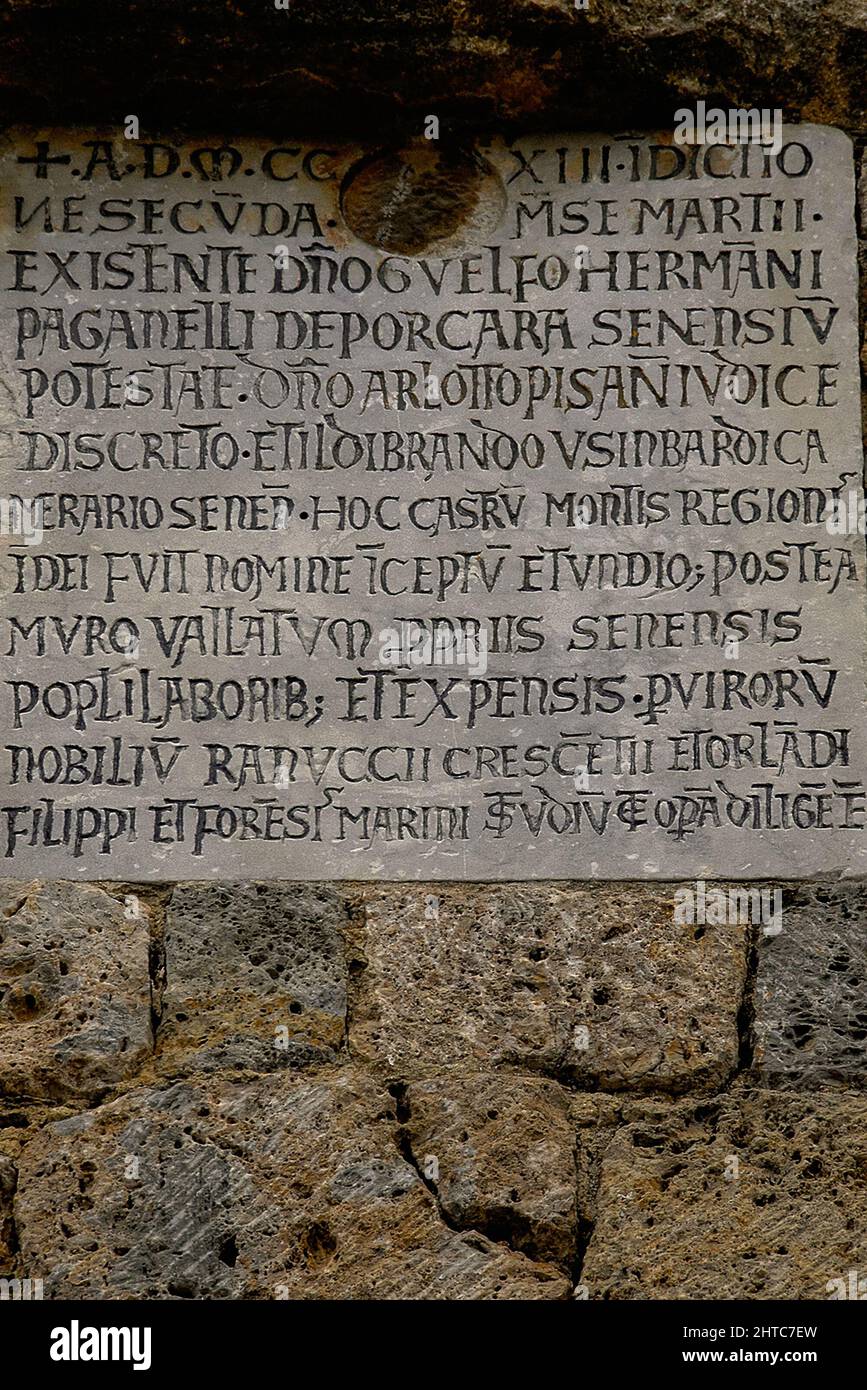 Lateinische Inschrift auf einer mittelalterlichen Tafel in Monteriggioni, einer ummauerten Stadt in der Toskana, Italien. Die Plakette befindet sich neben dem südlichen Tor von Monteriggioni, der Porta Romea oder Franca aus den frühen 1200s Jahren, und ist die Grundlage der Stadt Siena im Jahr 1213 als eine auf einem Hügel gelegene Zitadelle und ein nördliches Bollwerk gegen florentinische Truppen, die das Gebiet von Siena angreifen. Stockfoto