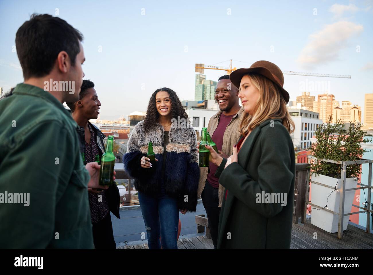 Multikulturelle Gruppe junger Erwachsener, die sich mit Getränken auf dem Balkon einer Dachterrasse in der Stadt unterhalten. Stockfoto