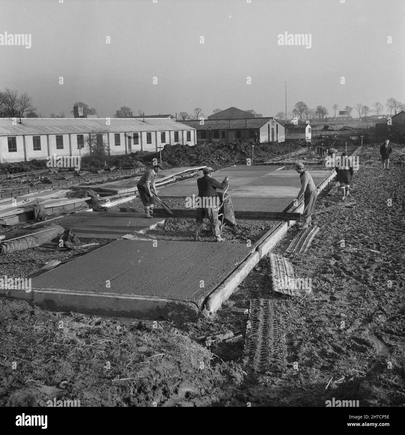 RAF Gaydon, Gaydon, Stratford-on-Avon, Warwickshire, 21/01/1953. Männer, die am Flugplatz Gaydon Bauarbeiten durchführen, gießen und nivellieren Beton während des Betonierens des Fußabdrucks eines Gebäudes. Anfang 1952 begannen die Arbeiten am Bau einer neuen Start- und Landebahn auf dem Flugplatz Gaydon. Es folgte ein zweiter Auftrag für den Bau von mehr als 100 Gebäuden der Easiform und des Luftverkehrsministeriums. Dazu gehörten ein Flugsicherungsturm, fünf Kesselhäuser, Luftwaffenhütten, Durcheinander und ein NAAFI. Das größte Easiform-Gebäude auf dem Gelände war ein Schulungszentrum mit einer Grundfläche von fast 3.000 Stockfoto