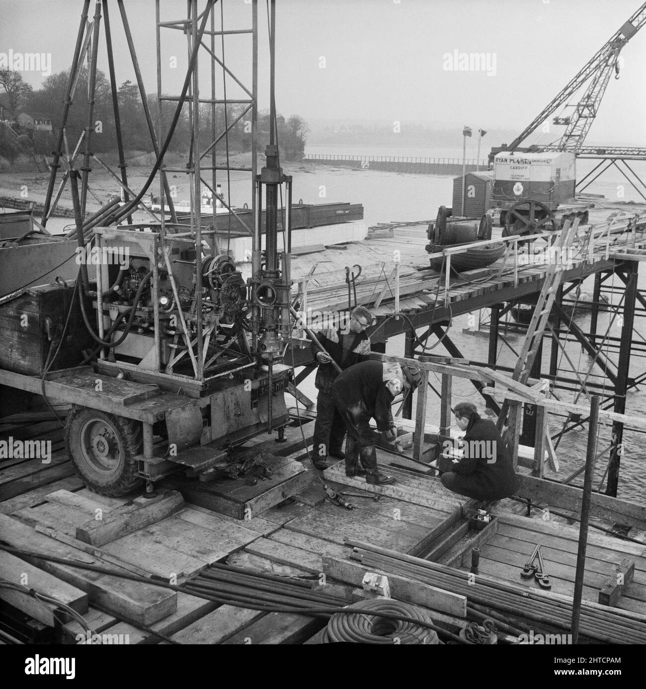 Severn Bridge, M48, Aust, South Gloucestershire, 12/12/1961. Die Arbeiter von Laing nutzen ein auf Lastwagen montiertes Bohrgerät auf den provisorischen Pontons am Standort der Fundamente für den Beachley-Turm der Severn Bridge. Dieses Foto wurde in der Januar 1962-Ausgabe von Team Spirit, dem Laing-Unternehmensnewsletter, mit der Überschrift „Ground Engineering Limited: Gesteinsbohrungen in Verbindung mit der Severn Bridge“ verwendet. Der Auftrag für den Bau der Fundamente für die Severn Bridge wurde von John Howard und Company gewonnen, aber ein Teil der Laing-Gruppe scheint für die Untersuchung beauftragt worden zu sein Stockfoto