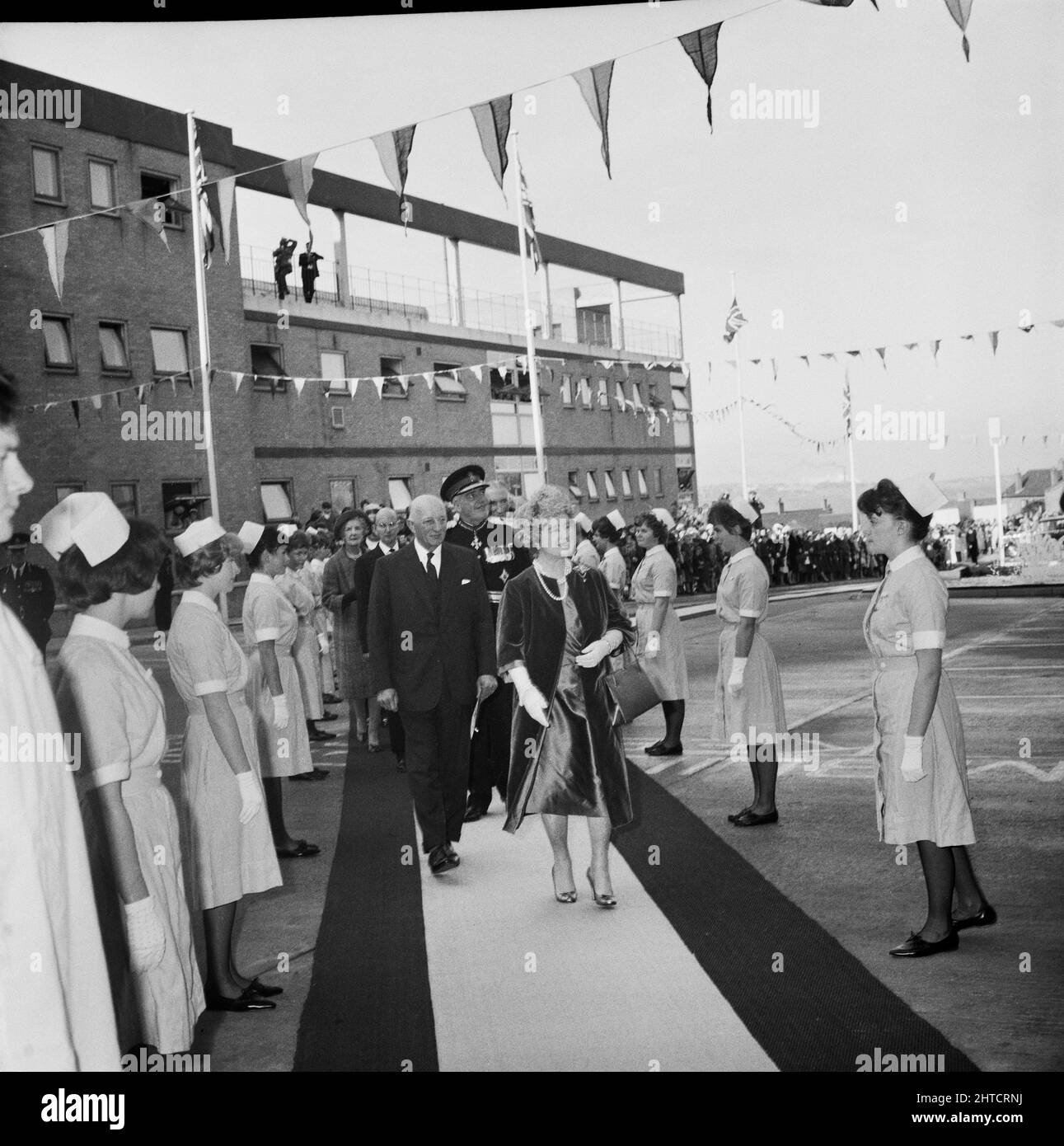 West Cumberland Hospital, Homewood Road, Homewood, Whitehaven, Copeland, Cumbria, 21/10/1964. Die Queen Mother und ihr Gefolge nähern sich dem Eingang des West Cumberland Hospital zur offiziellen Eröffnung. Der Prozessionsweg wird von Krankenschwestern und anderen Krankenhauspersonal flankiert. Stockfoto