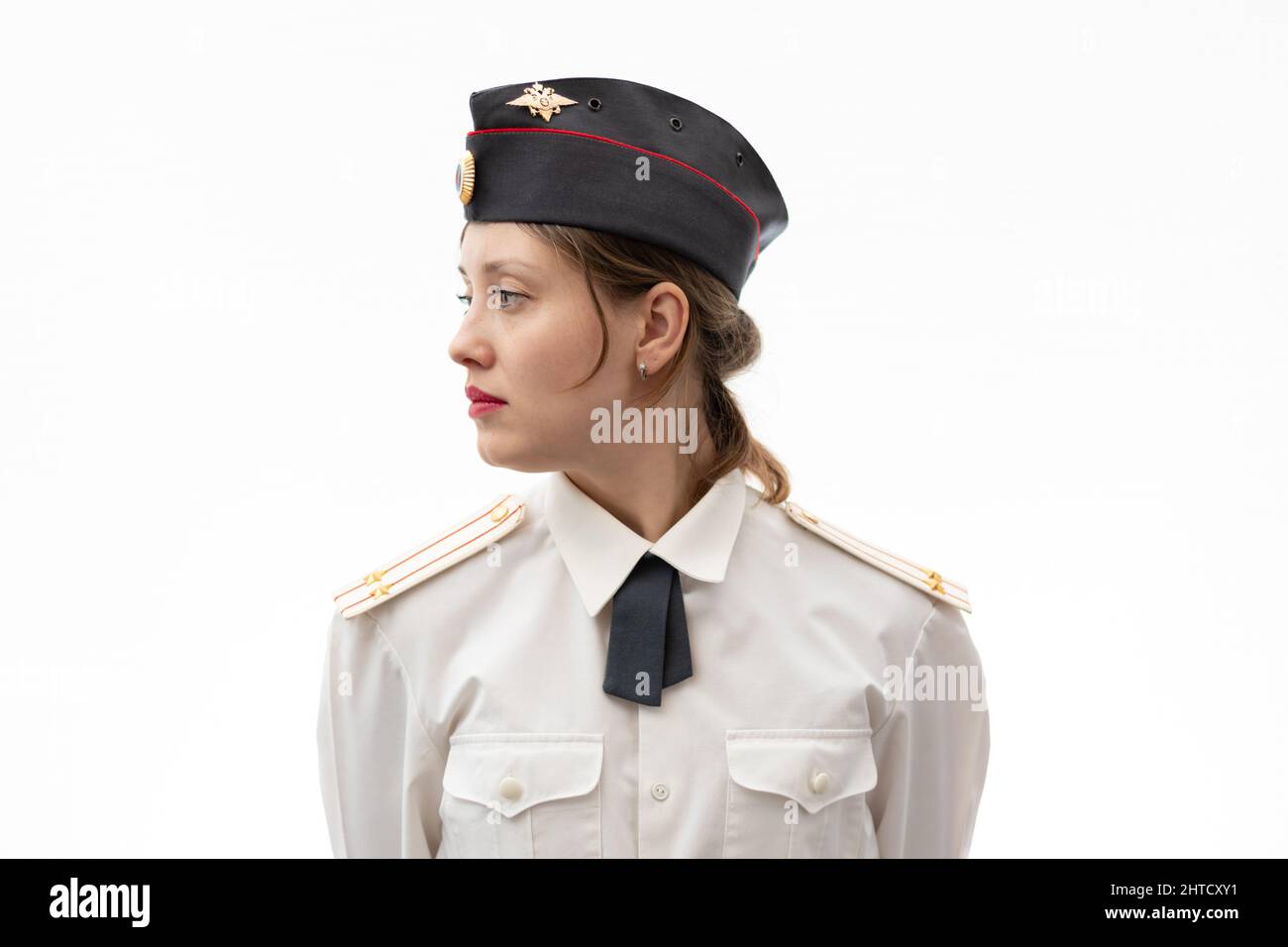 Eine schöne junge russische Polizist in Uniform in einer Mütze und Schultergurten eines Oberstleutnants und einem weißen Hemd auf einem weißen Bac Stockfoto
