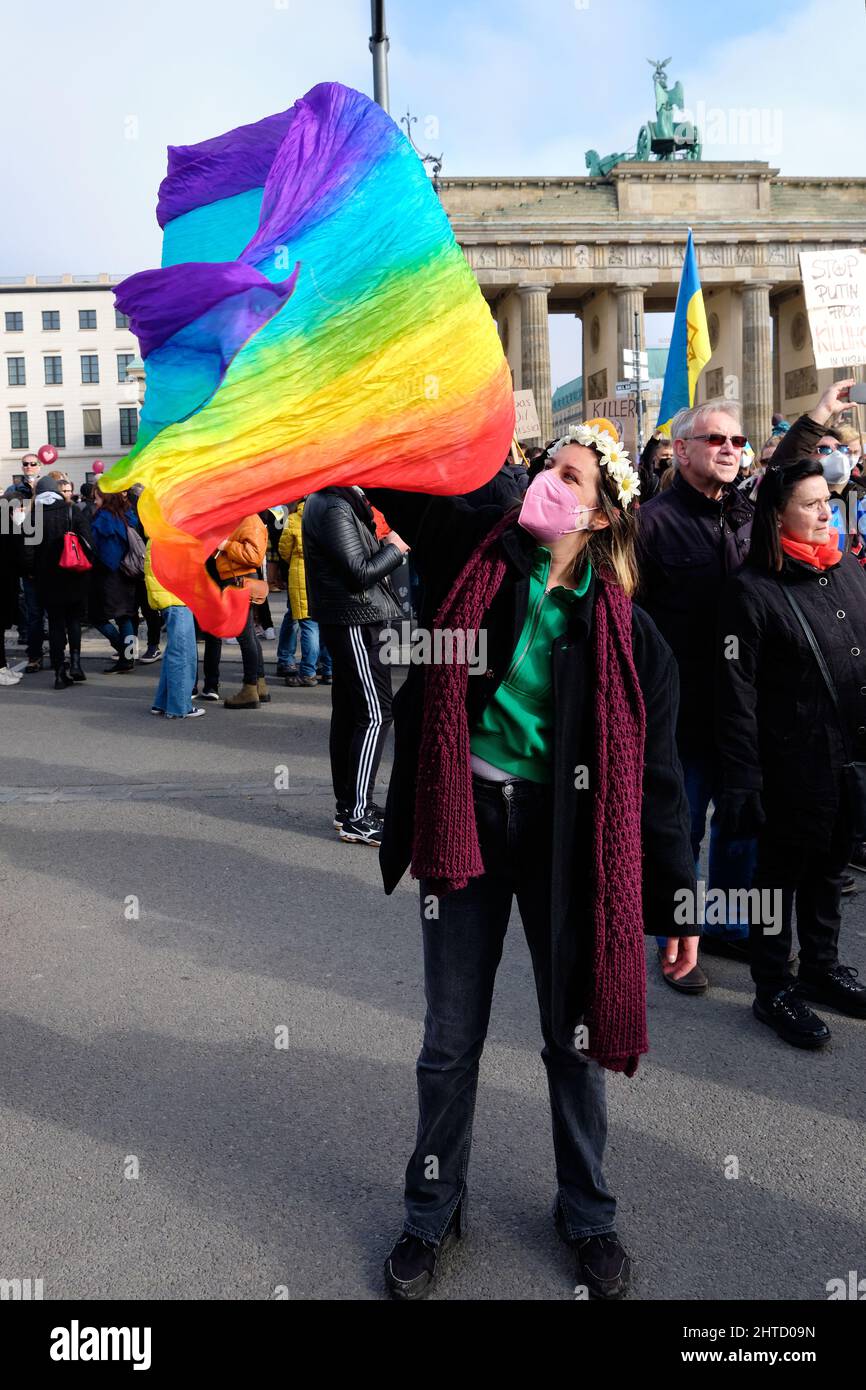 Frau in Gesichtsmaske mit Regenbogenfahne, Friedenssymbol. Menschen mit ukrainischen Fahnen und Plakaten protestieren gegen den Krieg in der Ukraine Stockfoto