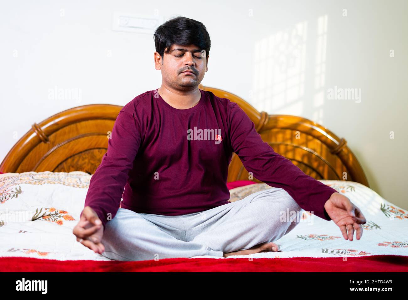 Junger indischer Mann, der Meditation mit geschlossenen Augen auf dem Bett macht – Konzept gesunder Lebensstile, Achtsamkeit und Strees Erleichterung Stockfoto