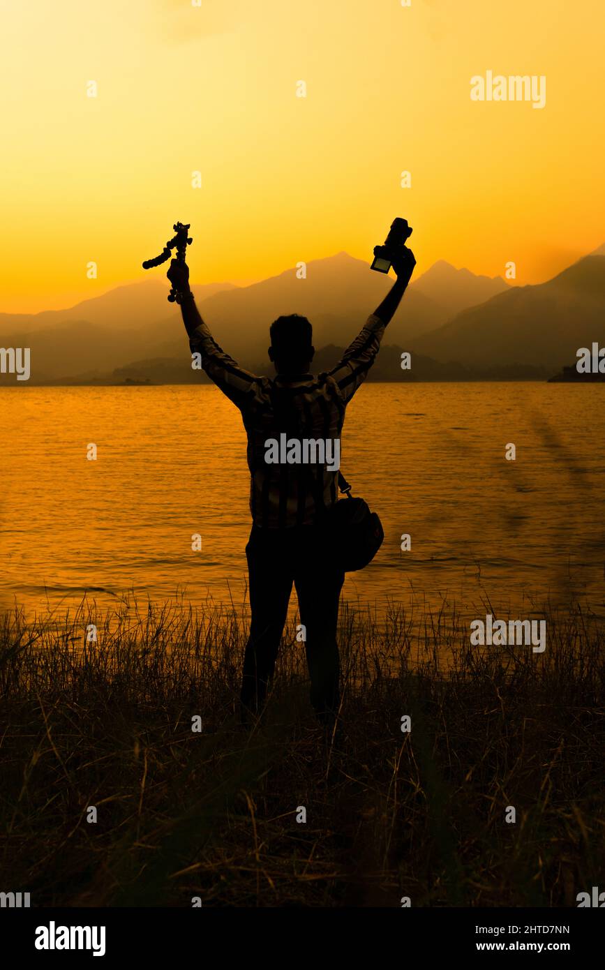 Naturfotograf halten Stativ mit Kamera, Reisende genießen wunderschöne Sonnenuntergänge, klicken Sie vom Banasura Dam Wayanad Kerala, World Photography Day Stockfoto