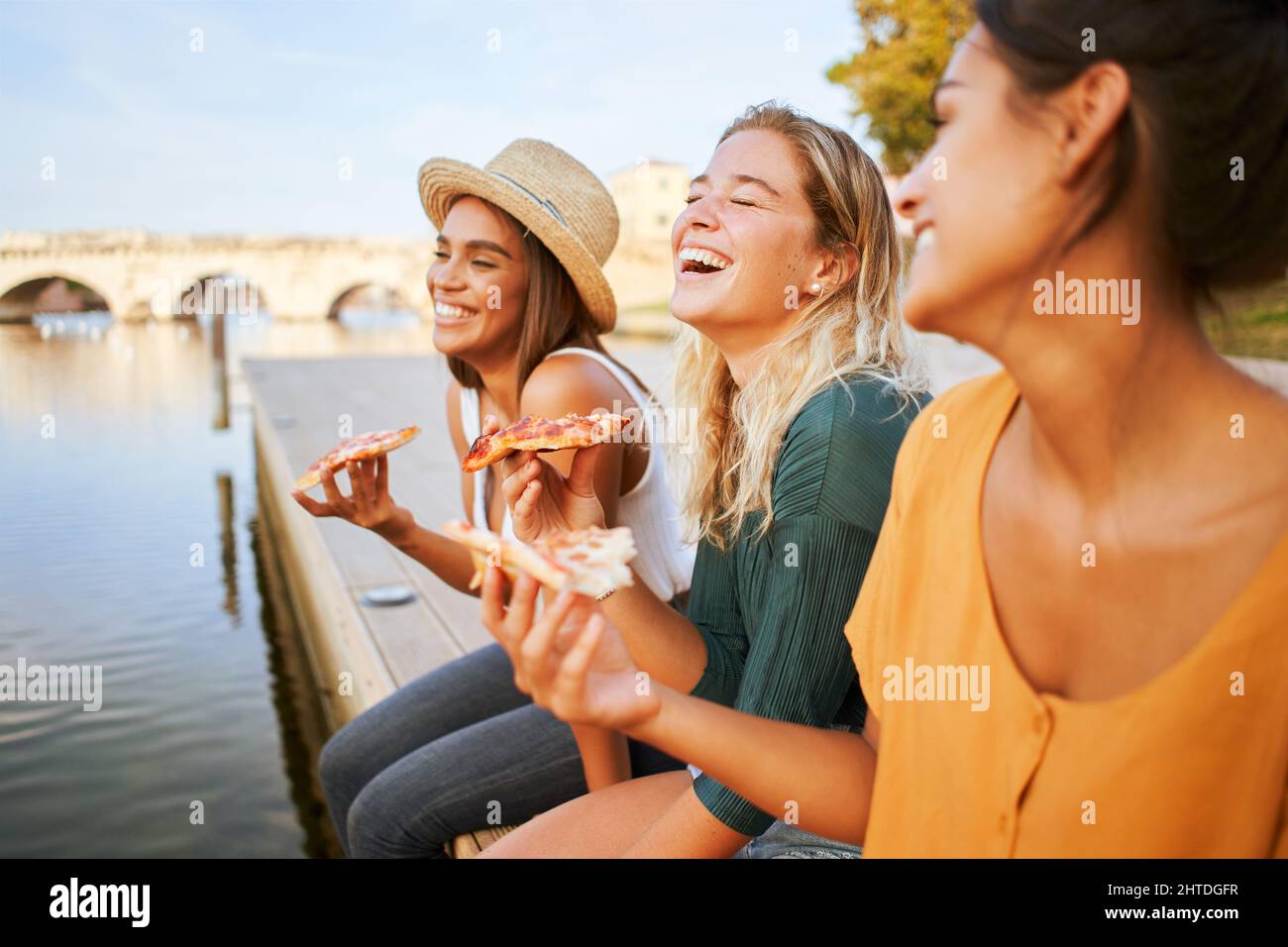 Drei schöne Frauen essen Pizza im Freien. Die glücklichen Mädchen genießen den Sommerurlaub am Wochenende zusammen. Stockfoto