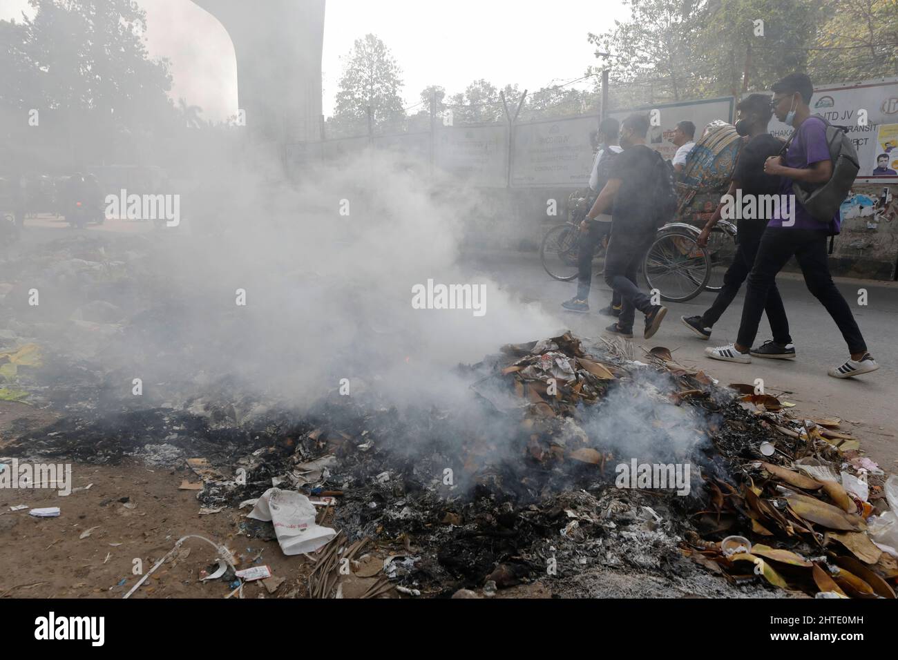 Dhaka, Bangladesch - 28. Februar 2022: Ein bangladeschischer Mensch geht an Rauchverbräuchen vorbei, die durch das Verbrennen von Abfallstoffen in einer Straße in Dhaka, Bangladesch, entstehen Stockfoto