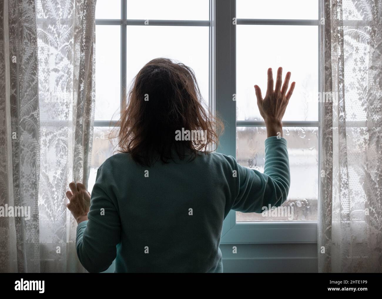 Frau, die am regnerischen Tag aus dem Fenster schaute. Konfuse Image; weibliche Depression, häuslicher Missbrauch, Menschenhandel, häusliche Gewalt, Psychische Gesundheit... Stockfoto