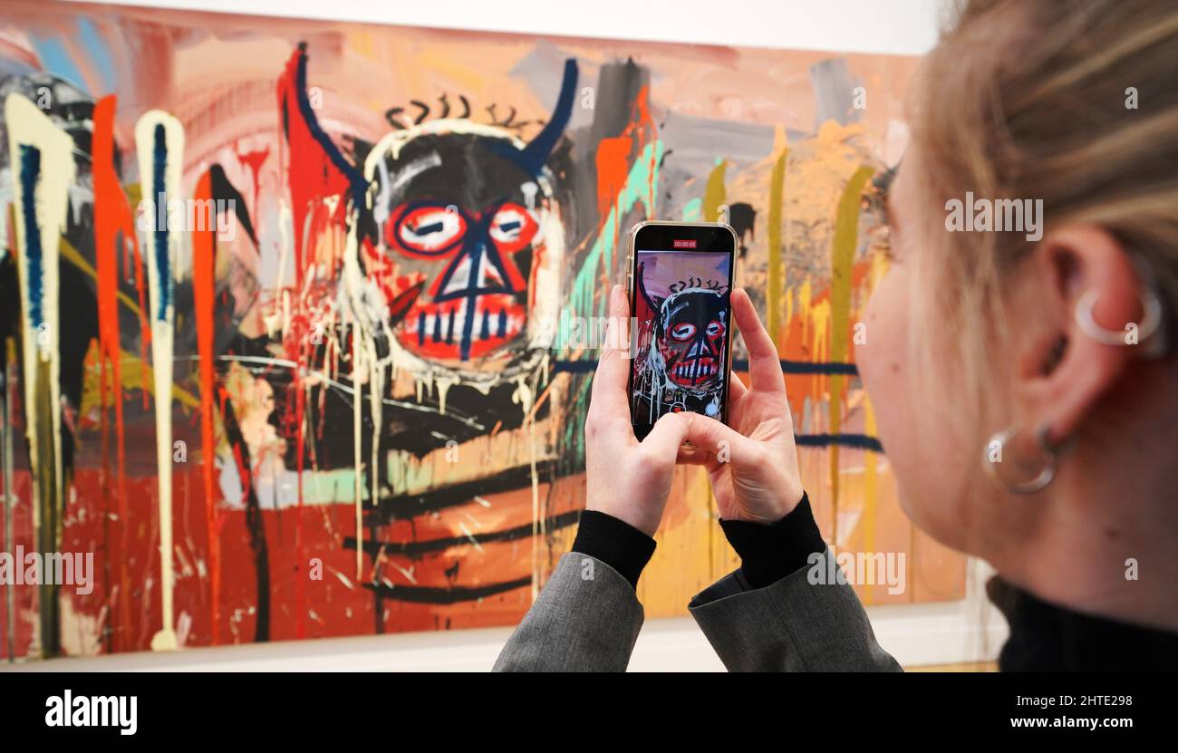 Ein Mitarbeiter der Galerie filmt ein Kunstwerk mit einer Höhe von 16 Metern und einer Breite von über 20 Metern, eines der größten Werke von Basquiat, wird im Phillips Auktionshaus in London enthüllt, bevor es mit einem geschätzten Wert von $70 Millionen versteigert wird. Bilddatum: Montag, 28. Februar 2022. Stockfoto