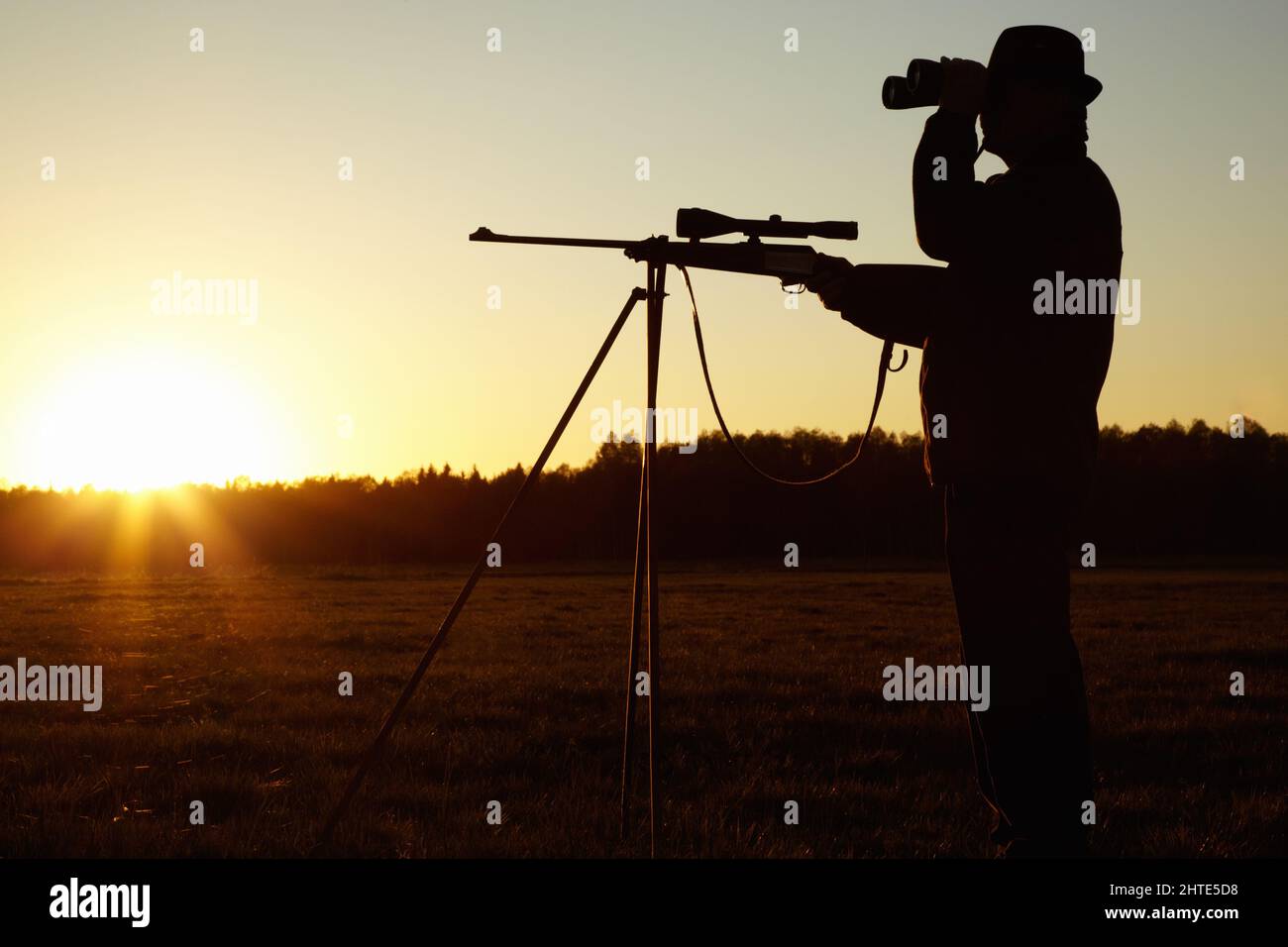 Auf der Suche nach. Eine Silhouette eines Mannes in der Tierwelt mit seinem Scharfschützengewehr bereit und Blick durch sein Fernglas. Stockfoto