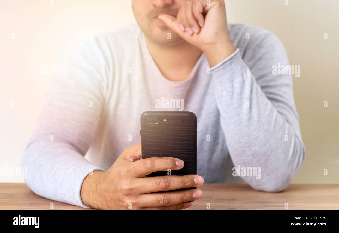 Mann hält Smartphone und schlägt seine Nägel aufgrund von Stress, Angst und besorgt. Stockfoto