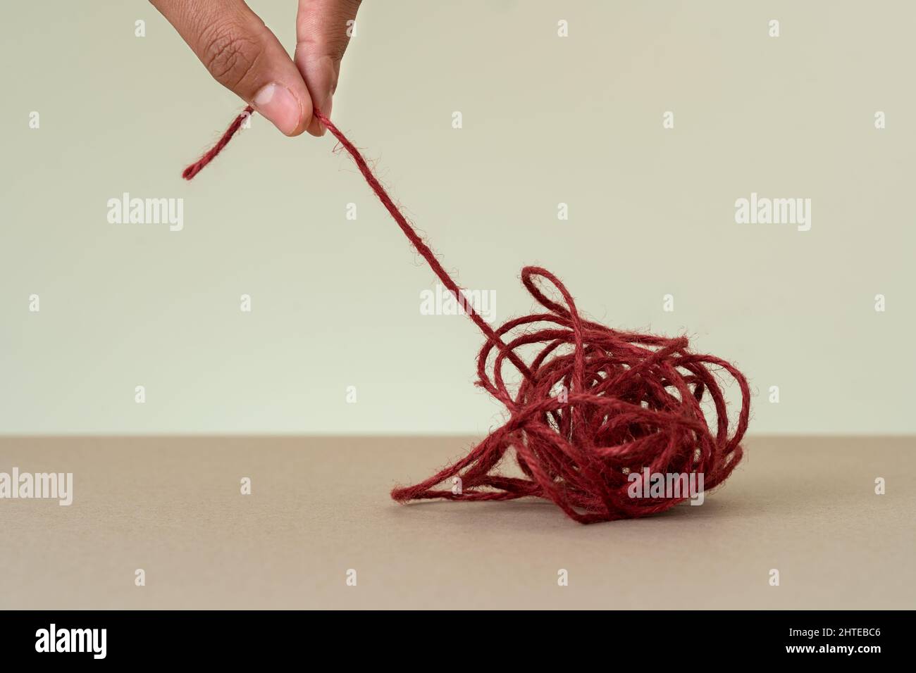 Nahaufnahme der roten Schleife und der Hand, die versucht, die Bindung zu lösen. Konzept der Fähigkeiten zur Problemlösung und Brainstorming zu konfuser Denkweise. Stockfoto