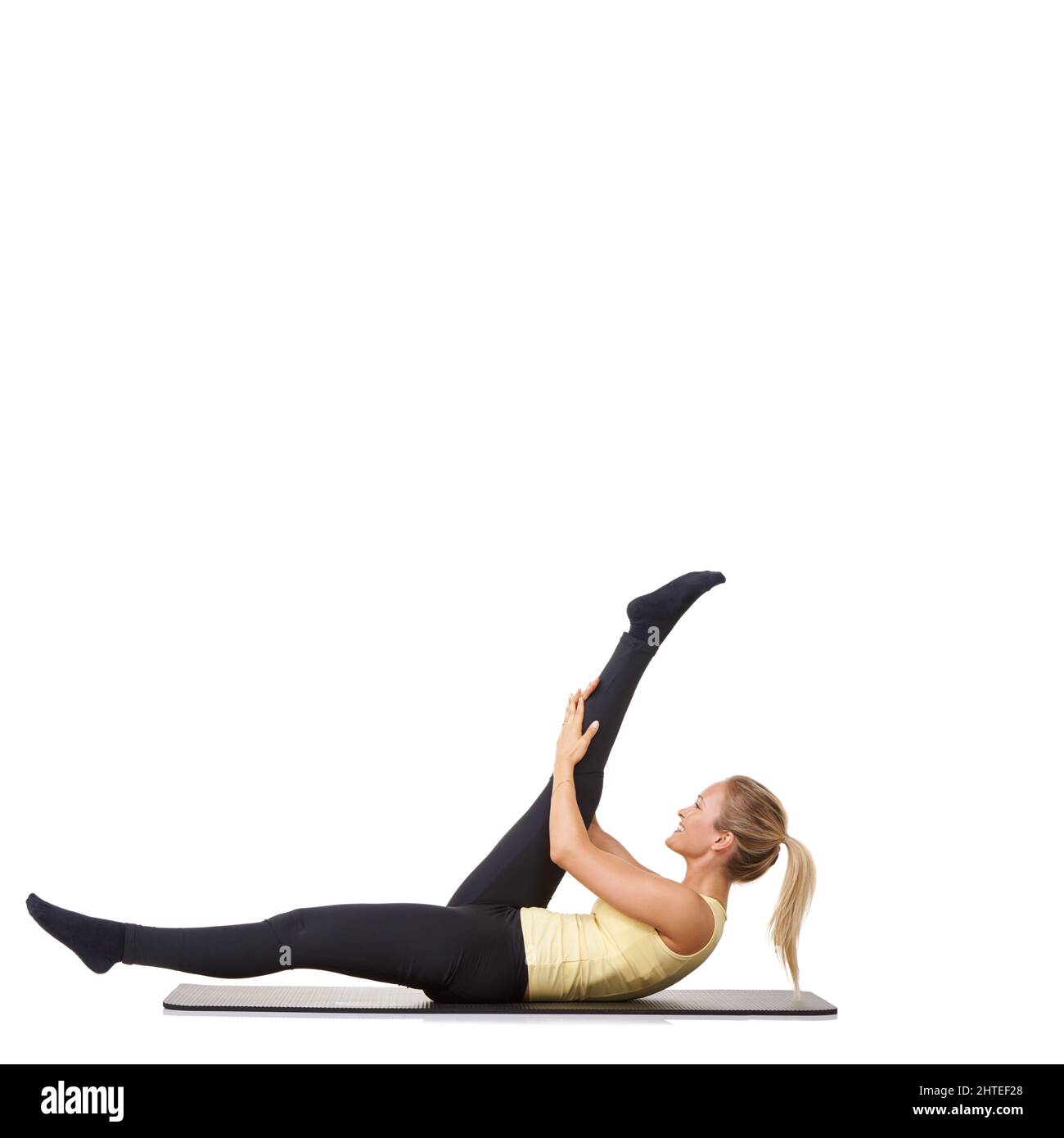 Alle ihre Muskelgruppen aufwärmen. Eine junge Frau, die ihre Beine auf einer Trainingsmatte ausstreckt - isoliert. Stockfoto