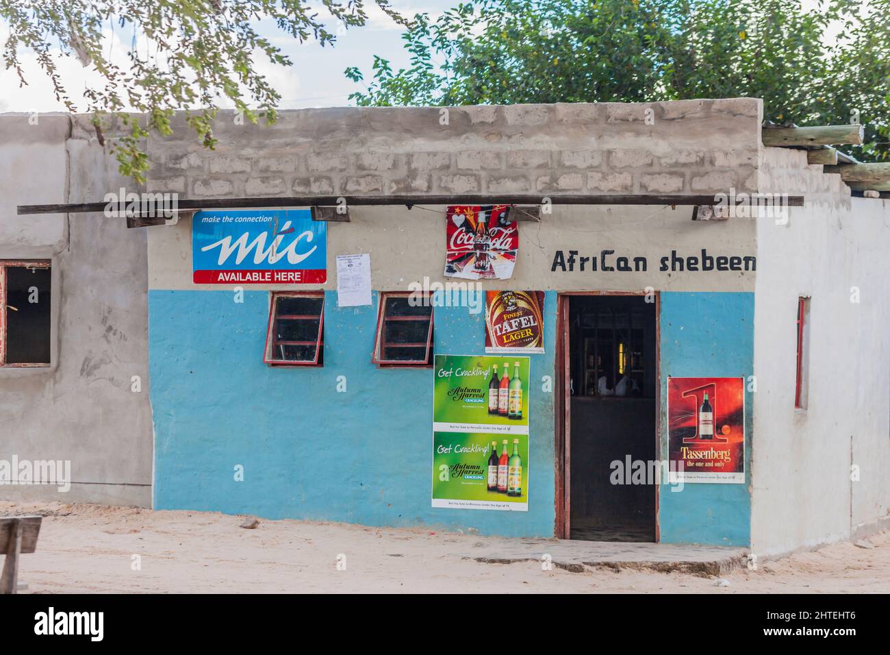 Ein 'African Shebeen', ein kleines Geschäft, das Alkohol verkauft, am Straßenrand im Norden Namibias, im südlichen Afrika. Der Ladenbesitzer steht hinter ihm Stockfoto