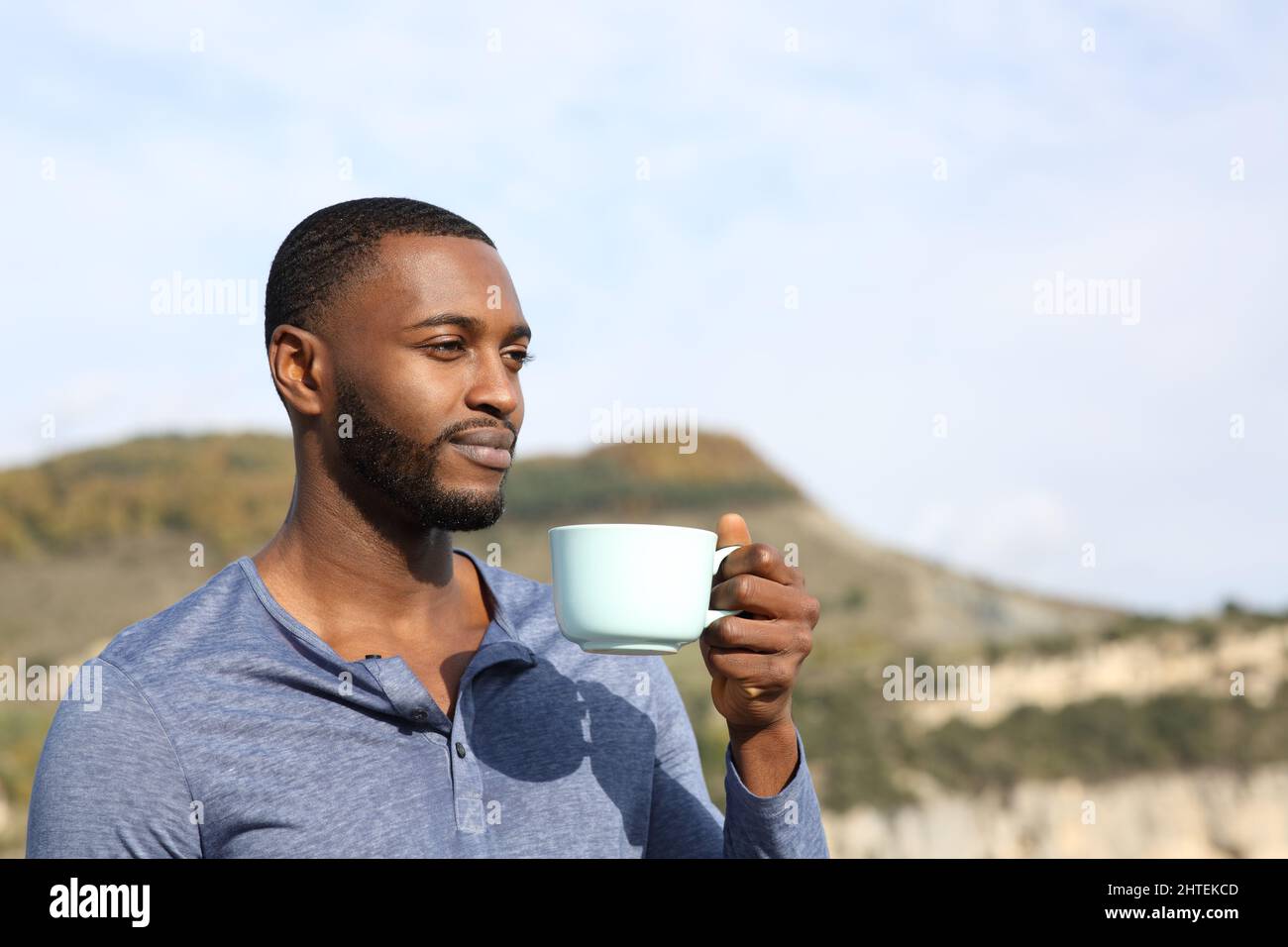 Mann mit schwarzer Haut trinkt Kaffee und kontempliert im Freien in der Natur Stockfoto