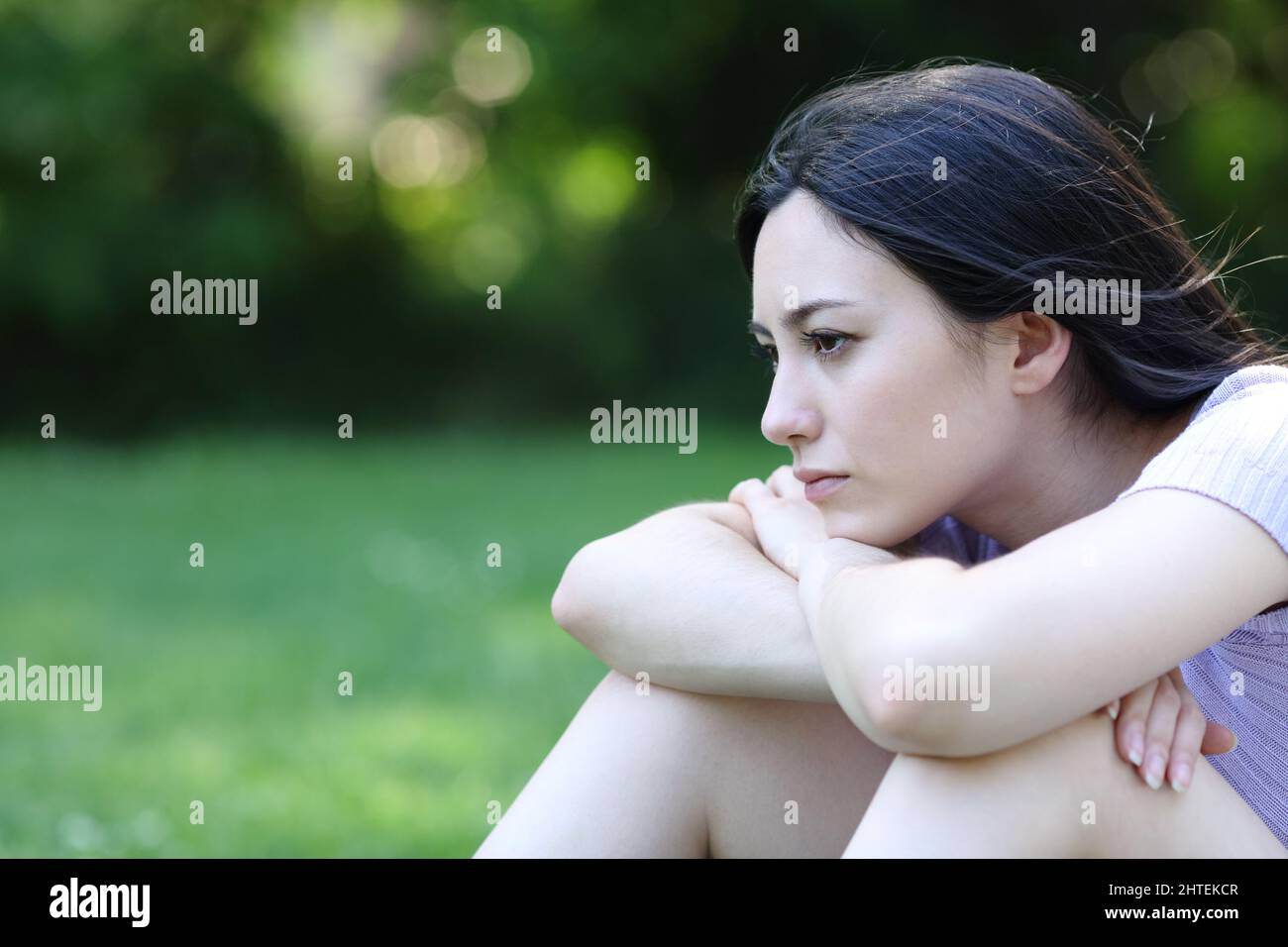 Traurige asiatische Frau, die sich beschwert, als sie allein in einem Park saß und wegschaute Stockfoto