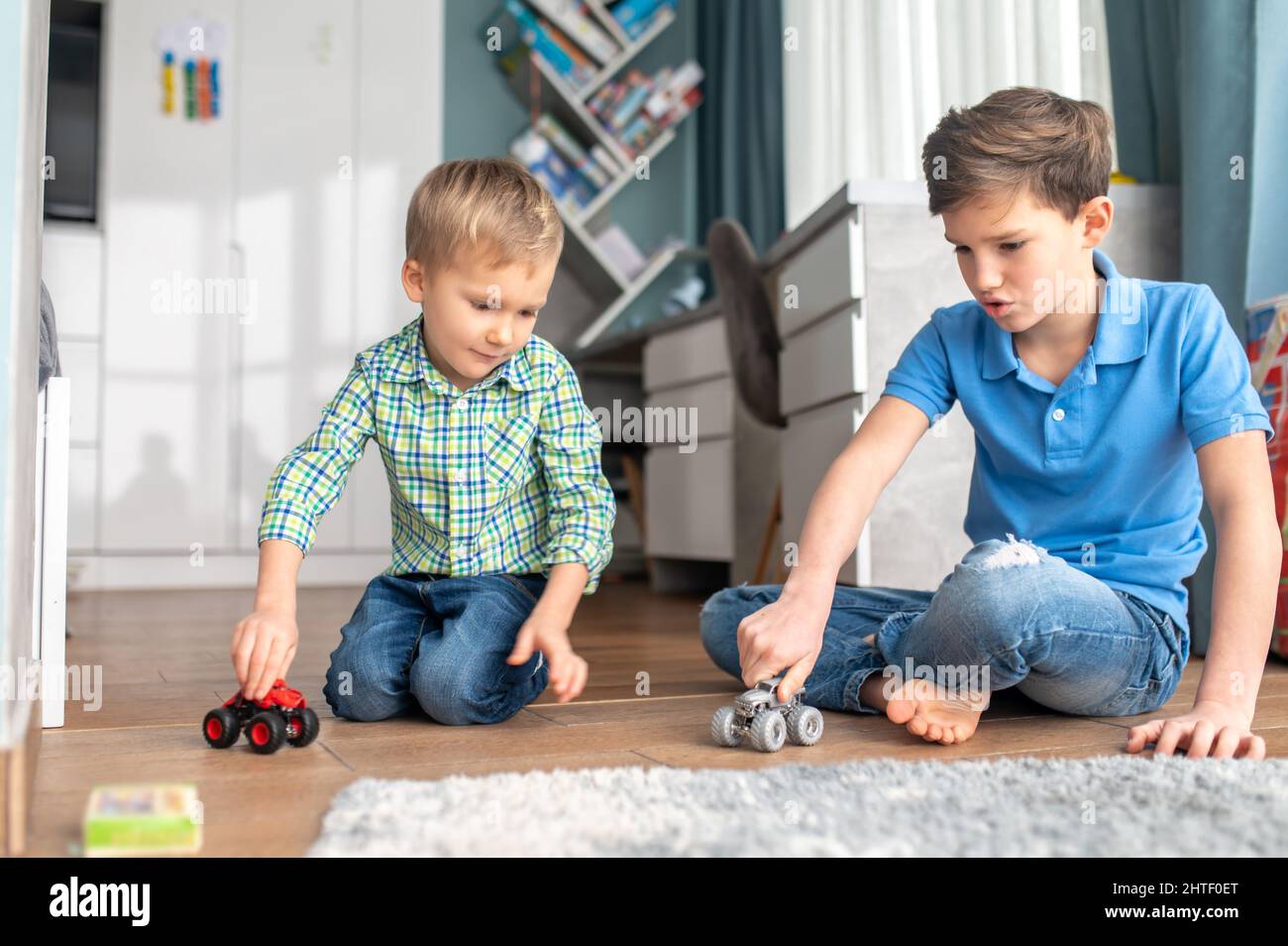 Zwei Geschwister, die drinnen mit Modellautos spielen Stockfoto