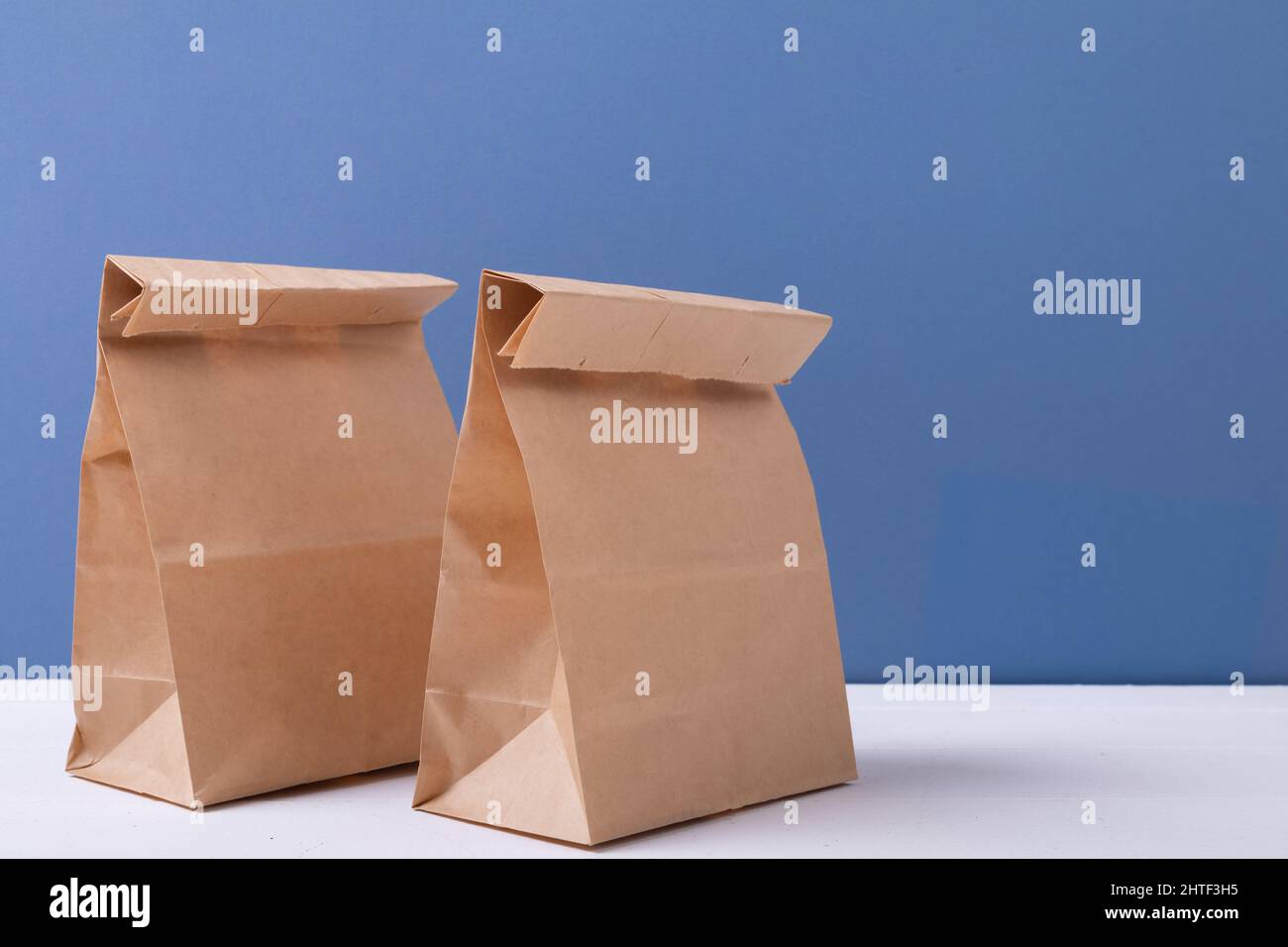 Nahaufnahme von braunen Papiertüten auf dem Tisch vor blauem Hintergrund mit Platz für Kopien Stockfoto