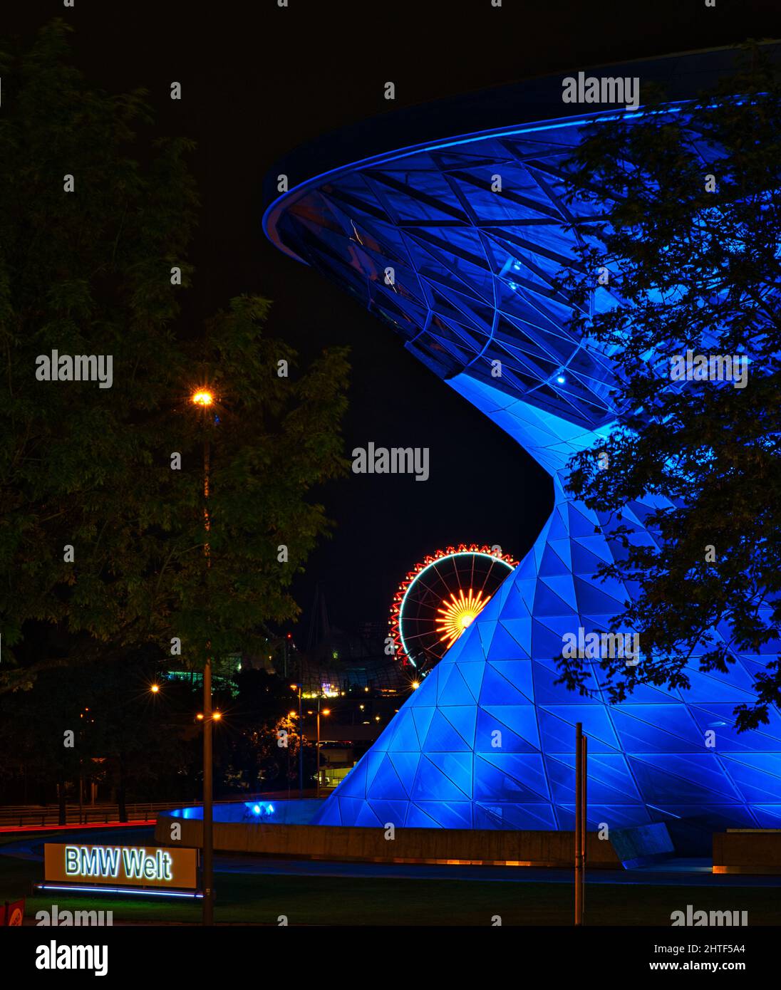 Die BMW Welt München als Teil der BMW Zentrale in München mit einem Riesenrad im Hintergrund blau beleuchtet Stockfoto