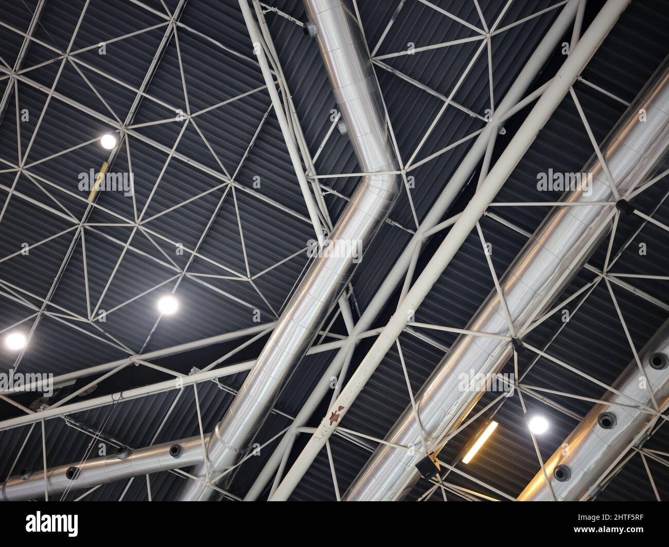 Decke einer Messe mit Röhren und Leuchten, die geometrische Strukturen bilden Stockfoto