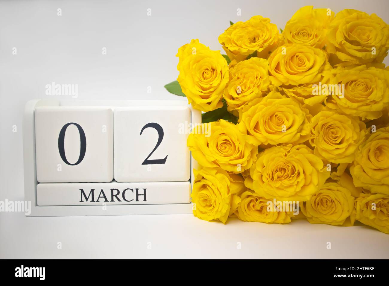 Holzkalender März 2 und gelbe Rosen auf weißem Hintergrund. Stockfoto
